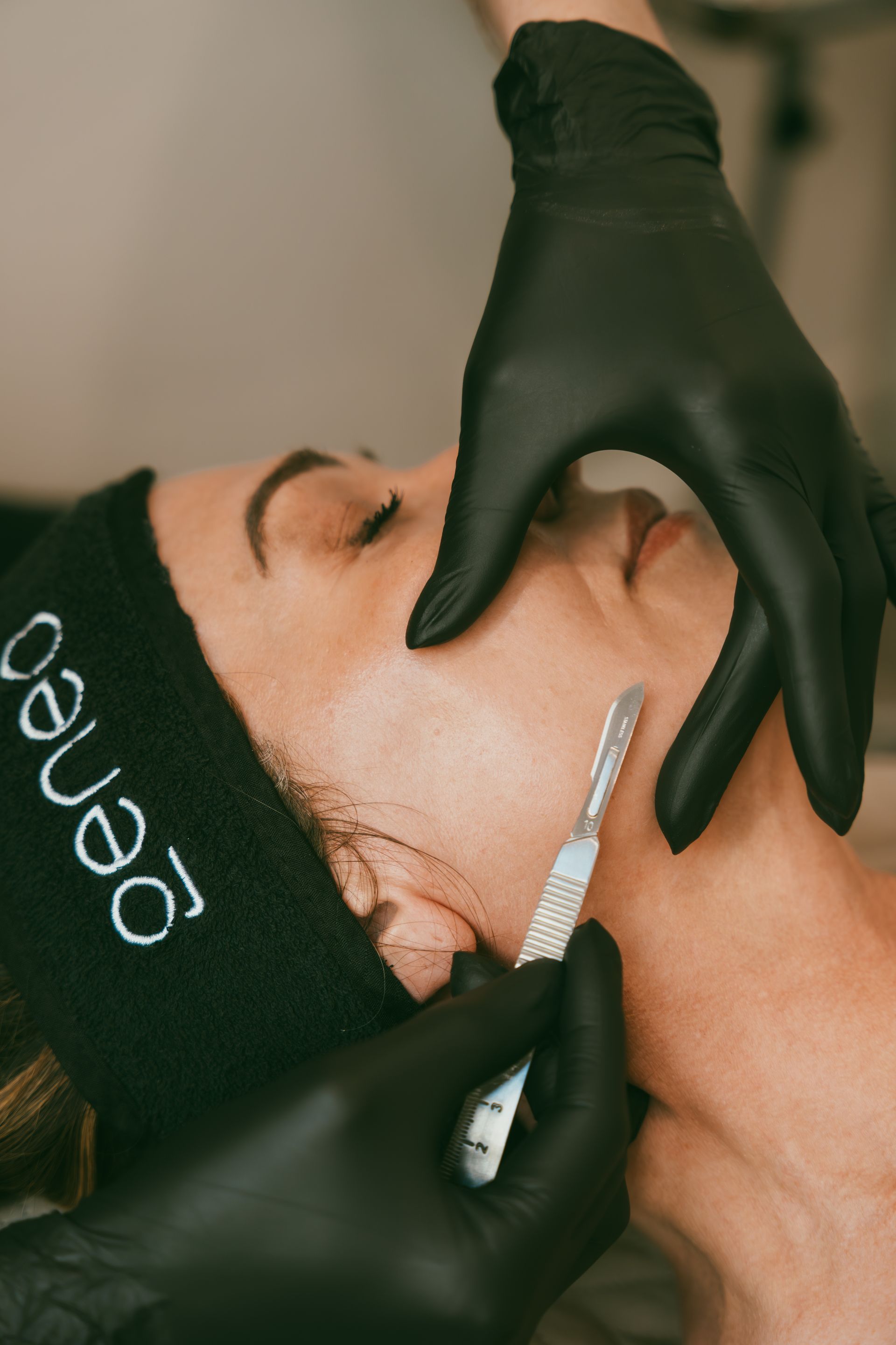 Gloved hands performing a facial skincare treatment on a client wearing a headband