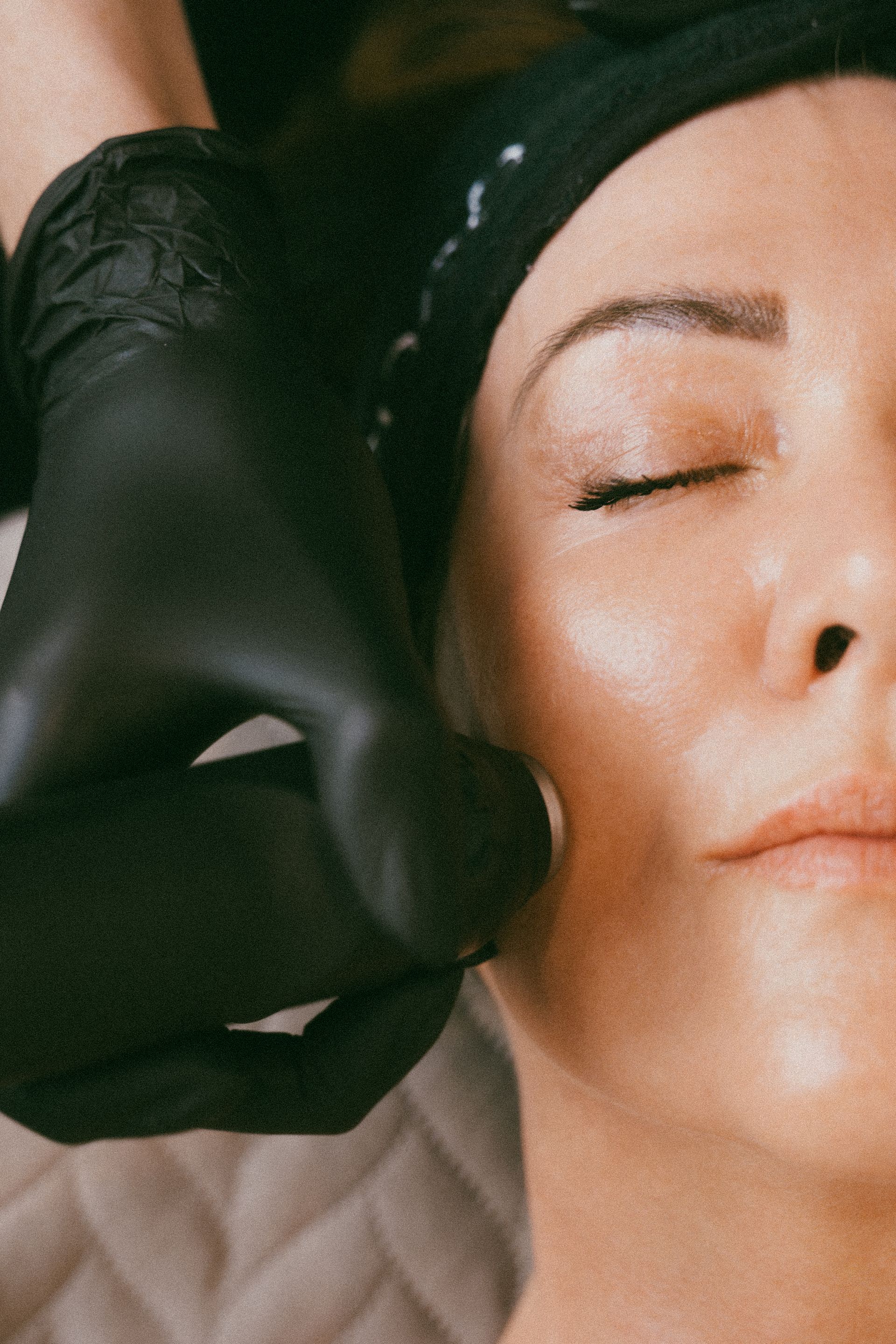 Close-up of a person receiving a black facial massage tool on their cheek with eyes closed