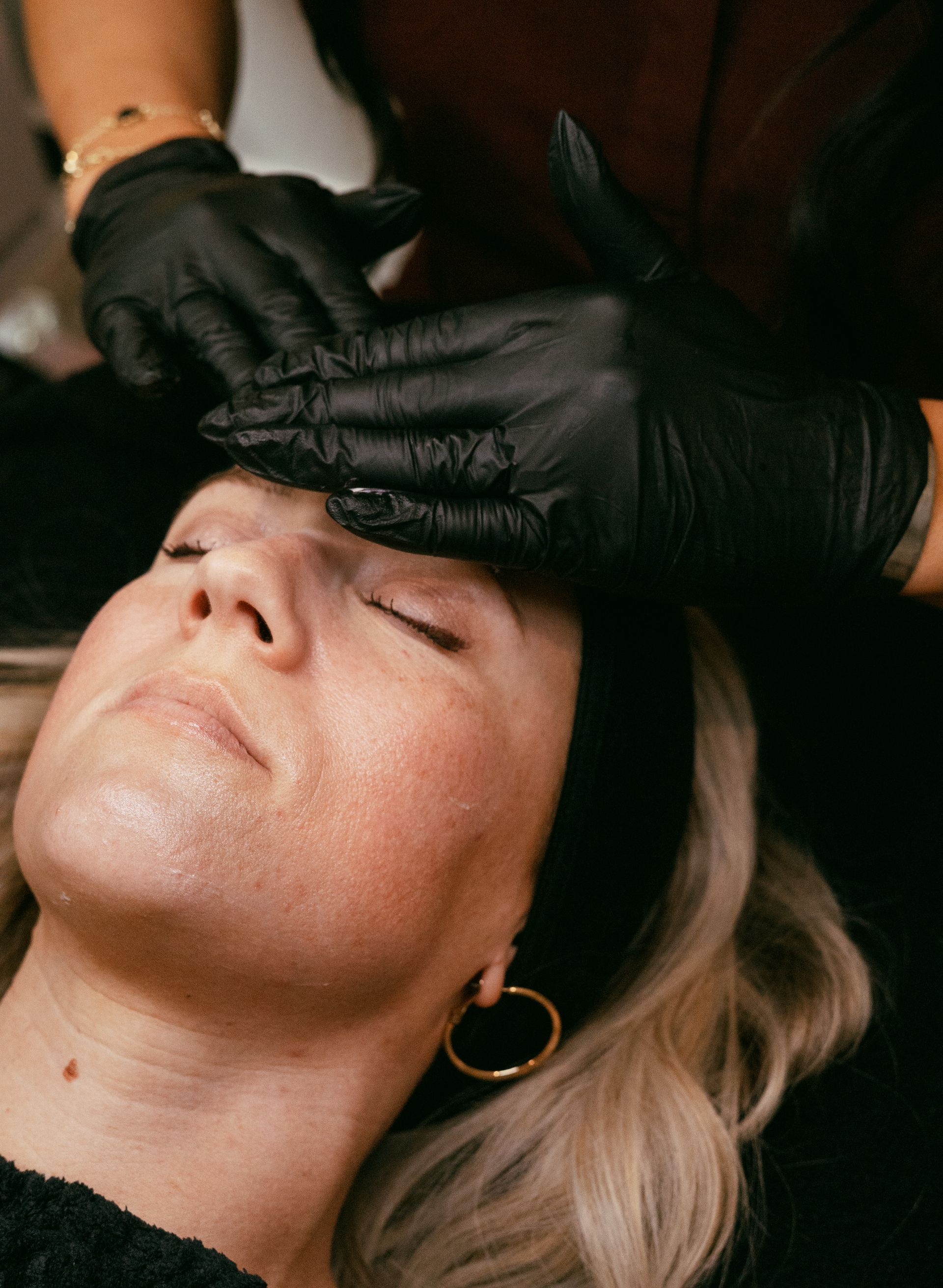 Gloved hands apply product to a woman’s forehead during a facial treatment