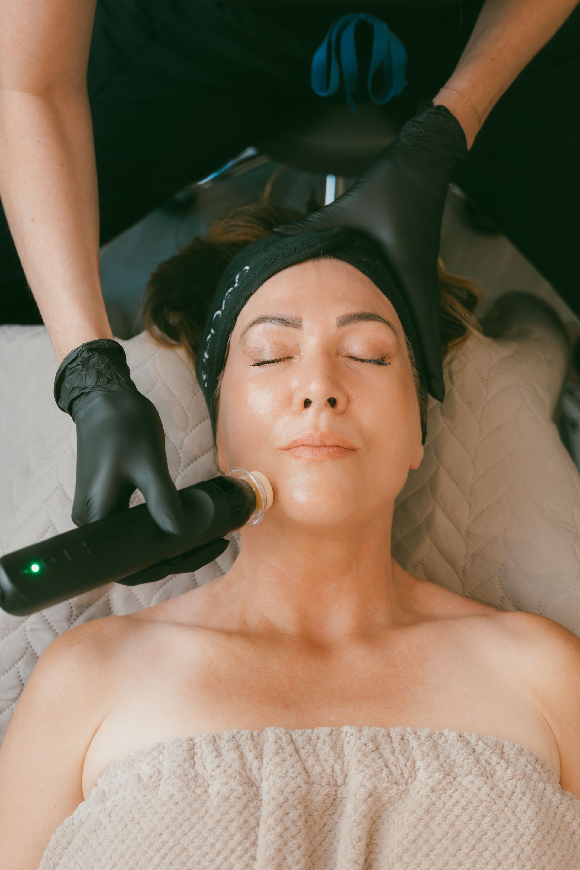 Facial treatment in progress as a practitioner uses a handheld device on a woman’s face.