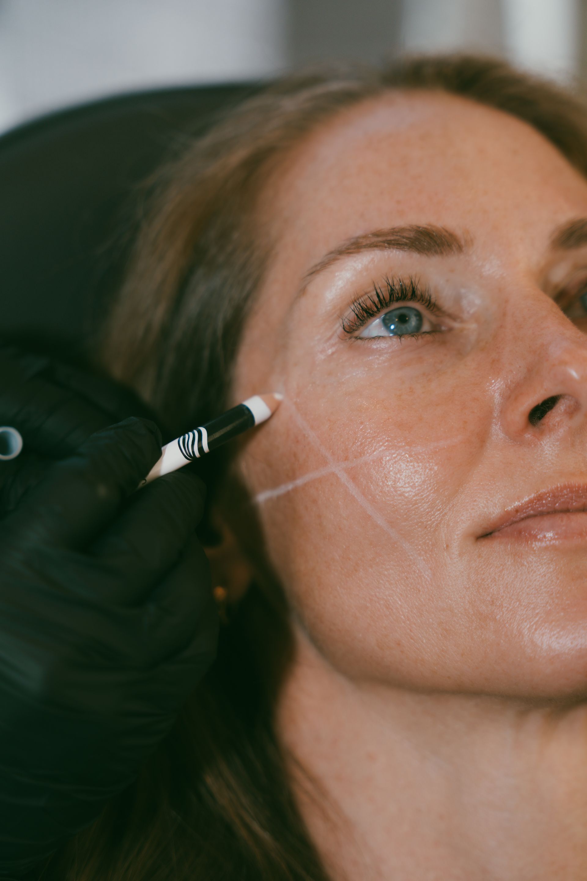 Gloved hand using a cosmetic applicator on a woman’s cheek during a facial treatment