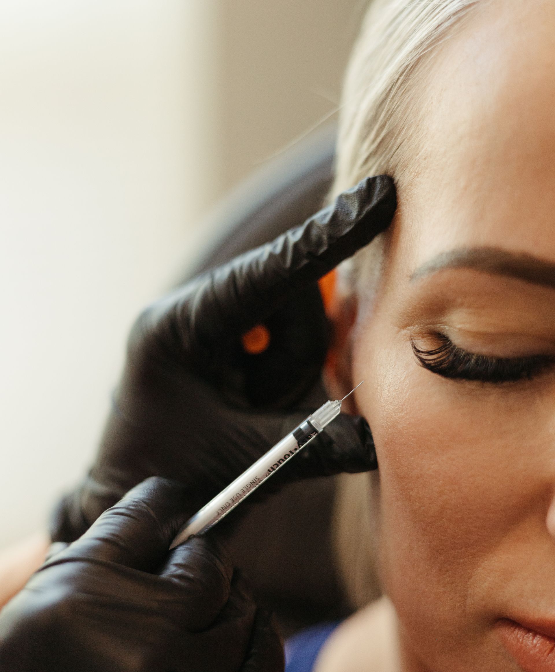 Gloved hands apply eyeliner to a woman’s closed eye