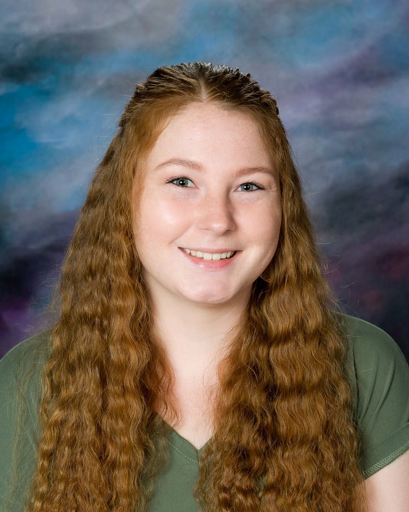 A young woman with long red hair is smiling for the camera.