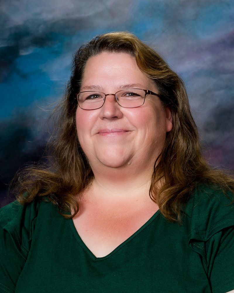 A woman wearing glasses and a green shirt is smiling for the camera.