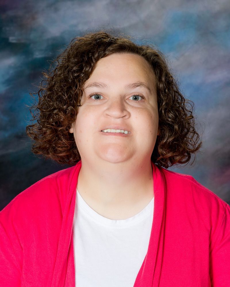 A woman with curly hair is wearing a pink sweater and a white shirt.