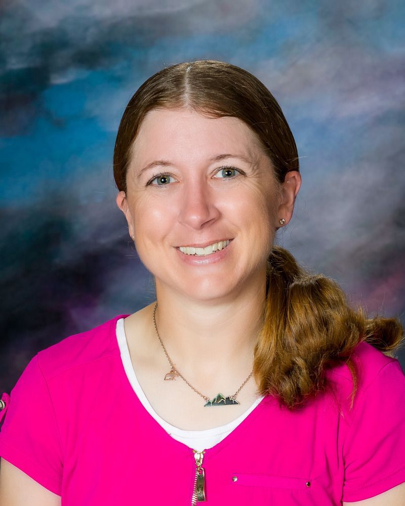 A woman wearing a pink shirt and a necklace is smiling for the camera.