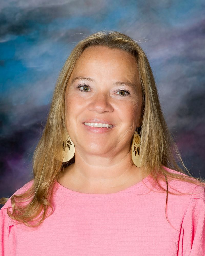 A woman in a pink shirt and earrings is smiling for the camera.
