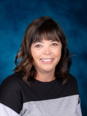A woman is smiling for a picture in front of a blue background.