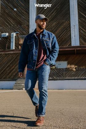 A man wearing a denim jacket and hat is walking down a street.