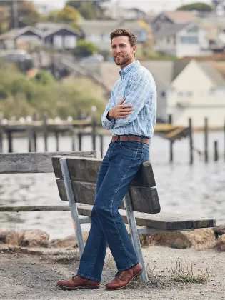 A man is standing on a wooden bench next to a body of water.