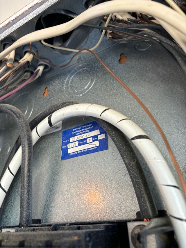 Close-up of tangled white and black cables inside a gray metal compartment with a blue label.