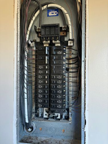 Open electrical breaker panel in a narrow wall alcove with many labeled switches and wires.
