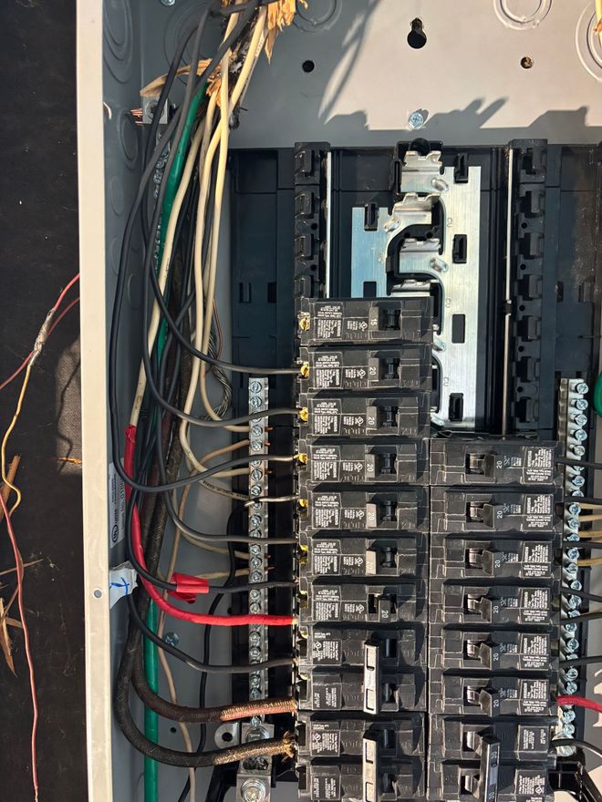 Open electrical breaker panel with exposed wires and rows of circuit breakers in a wall cavity