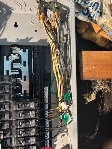 Damaged electrical panel with exposed wires and debris inside a wall opening