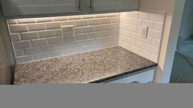 Kitchen countertop with speckled granite, white subway tile backsplash, and under-cabinet lighting