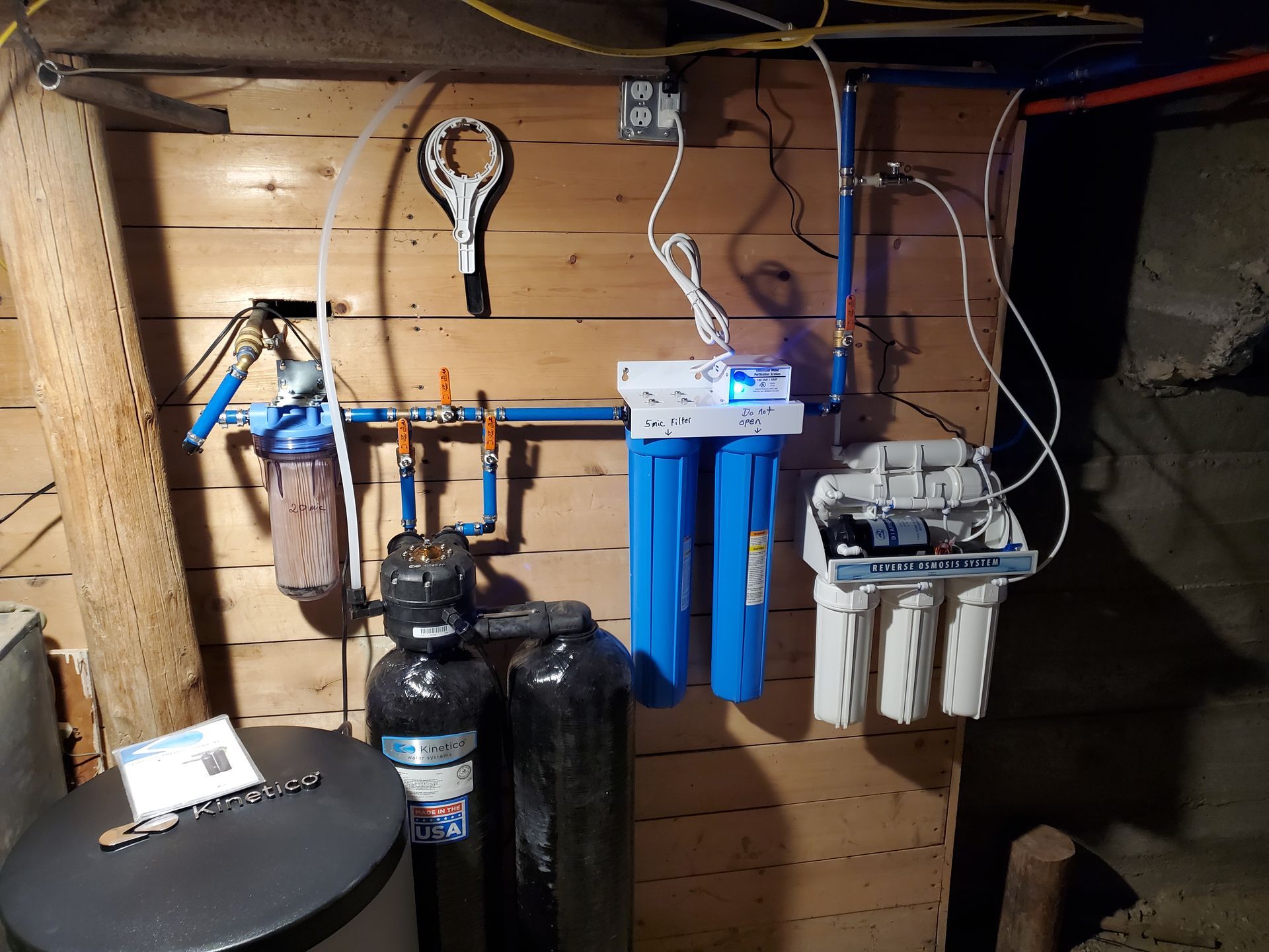 Water filtration system with various filters and tanks mounted on wooden wall.