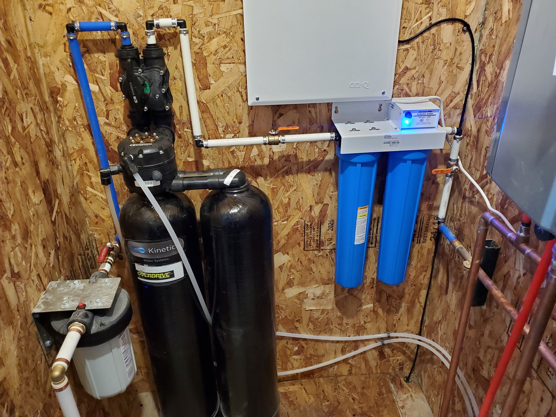 Water filtration and softening system installed on a wood panel wall with blue and black components.