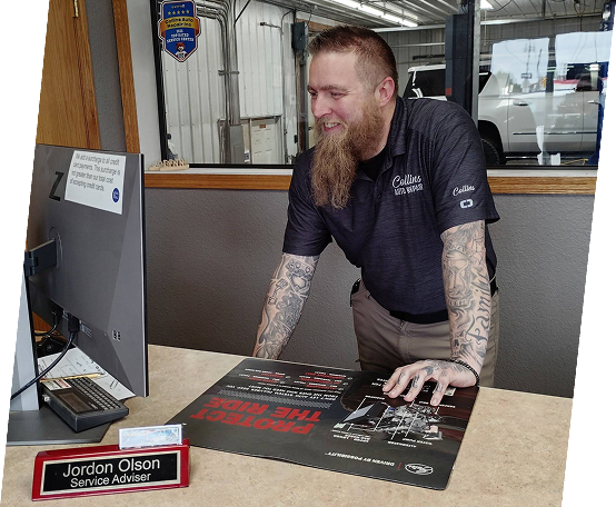 Tattooed man in dark polo leaning over a desk at a booth, smiling beside a computer monitor and display items