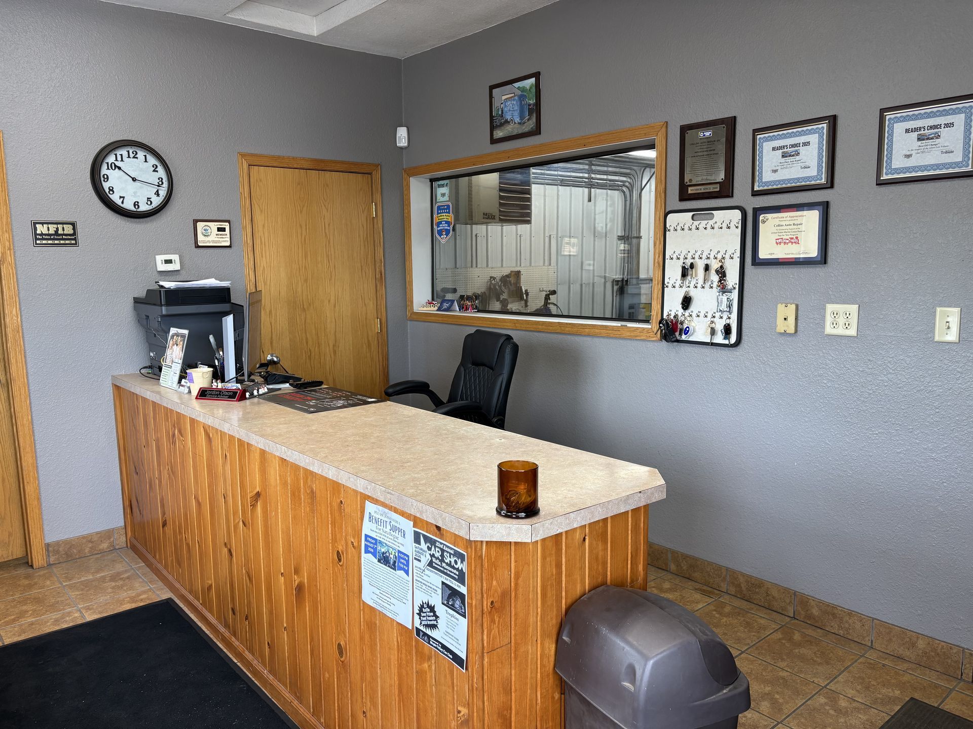 Office reception desk with wood counter, gray walls, clock, certificates, and wall window.