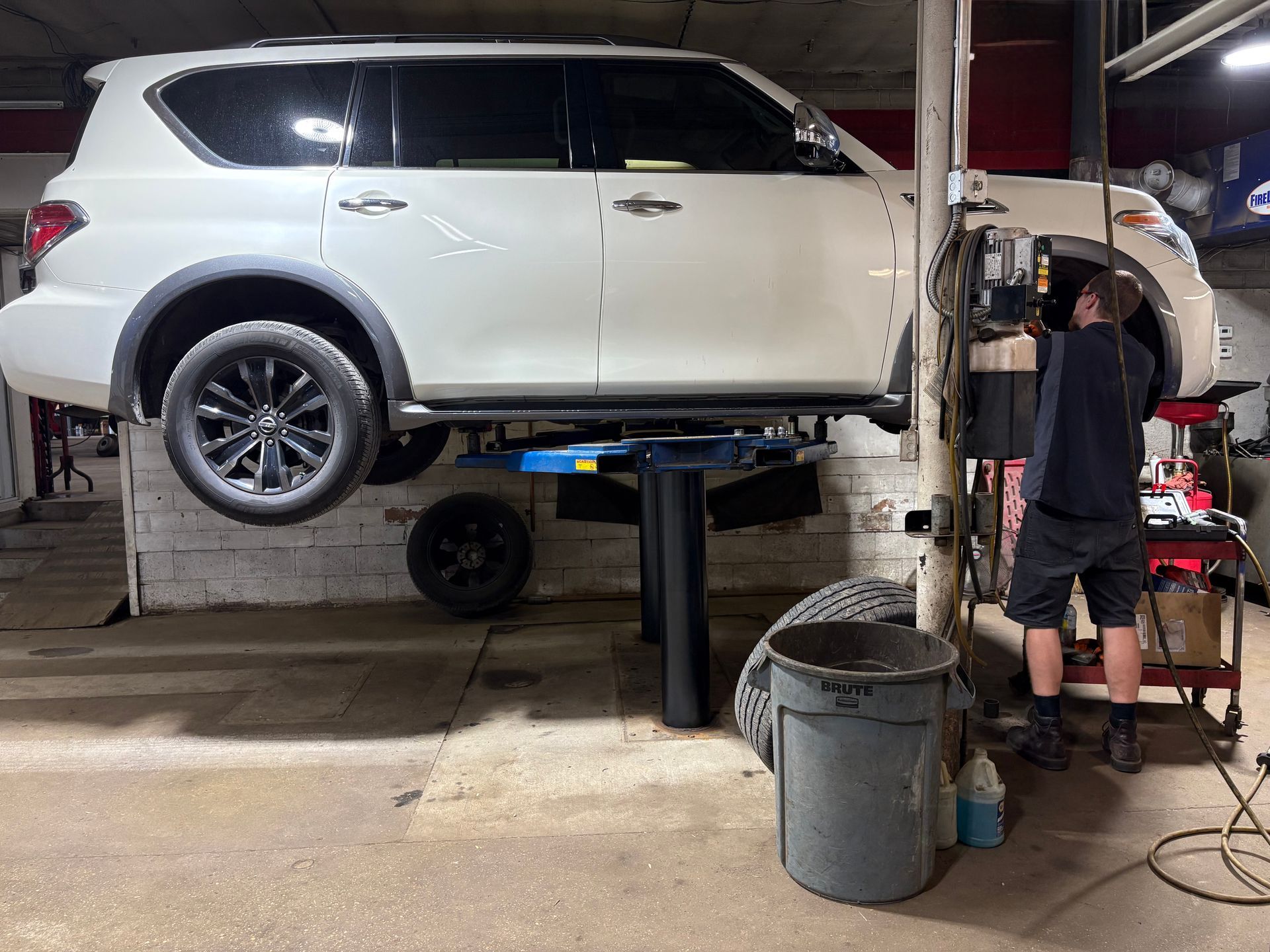 White SUV on a lift in an auto shop while a mechanic works beside it.