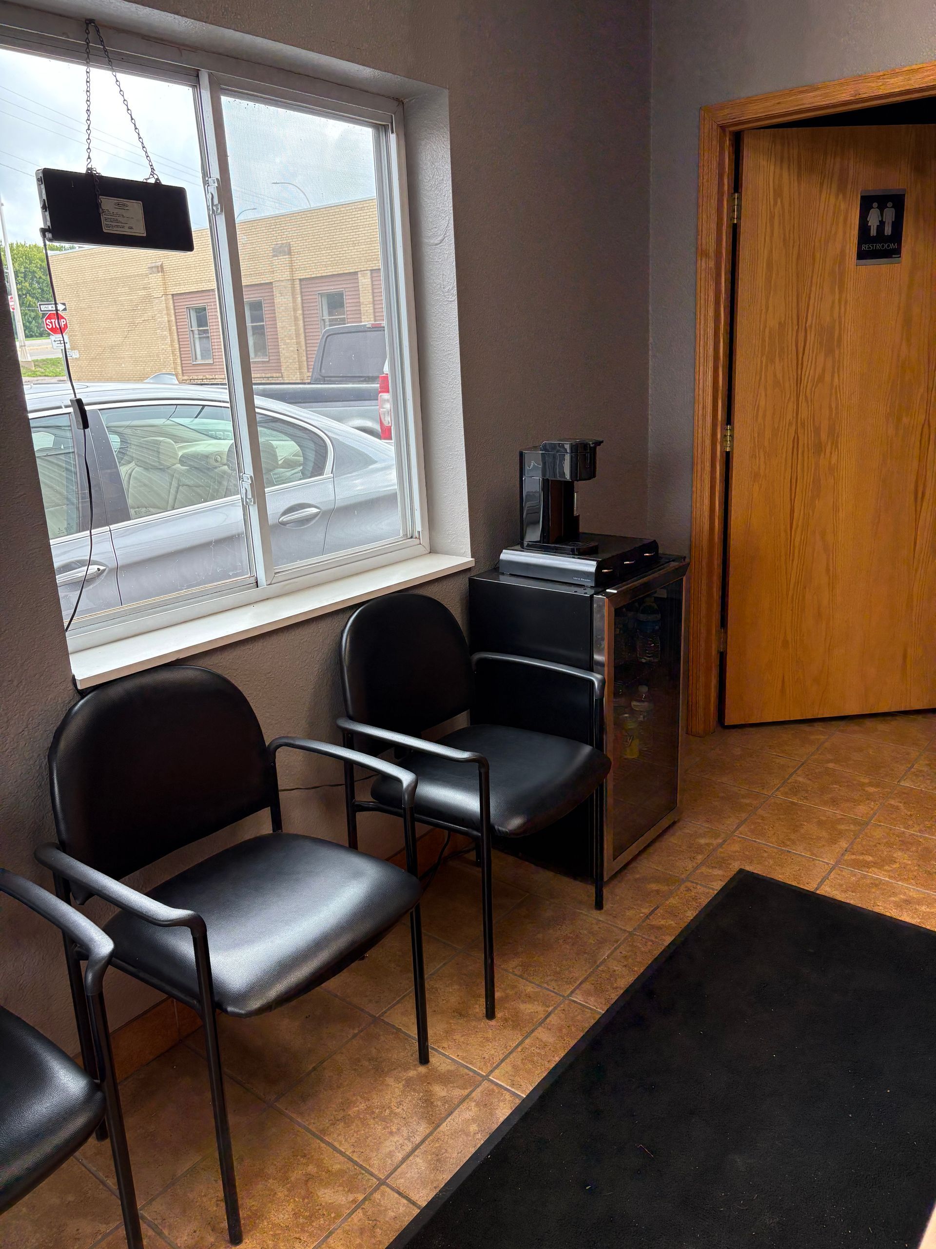 Waiting room with black chairs, a small table, a window, and a restroom door