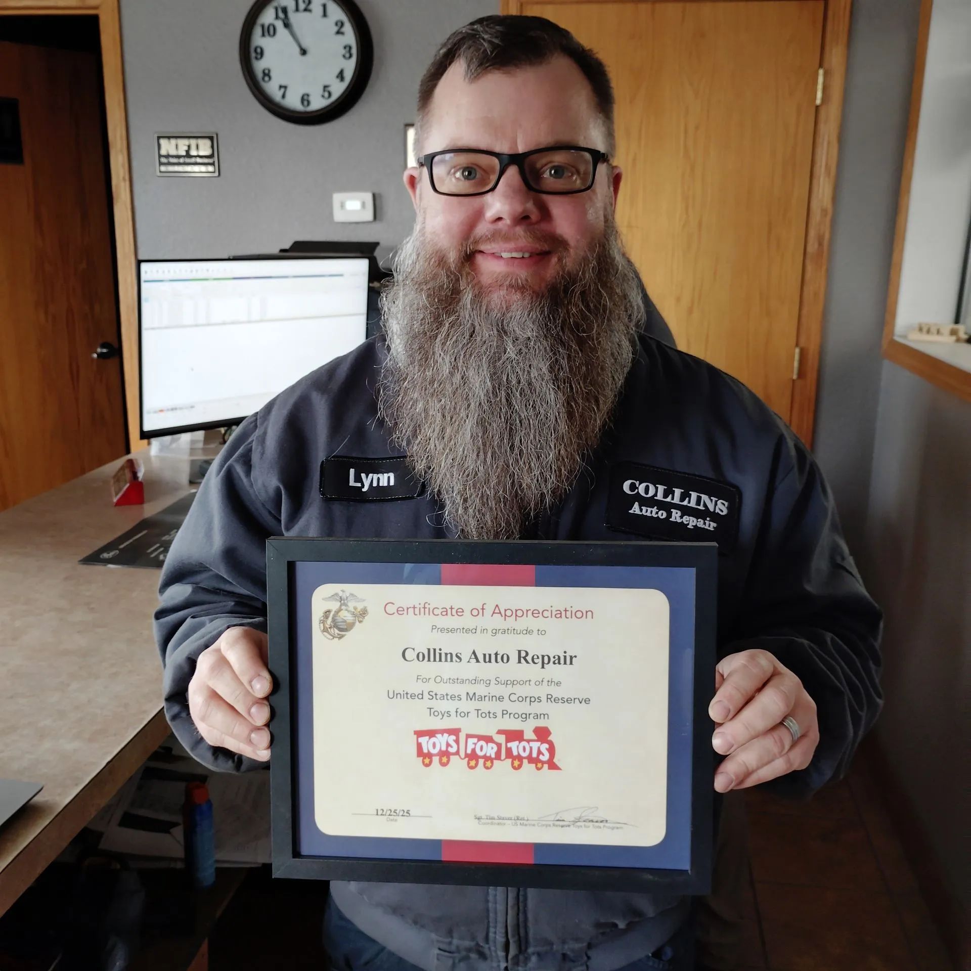 Man holding a framed certificate in an office, smiling behind a desk.