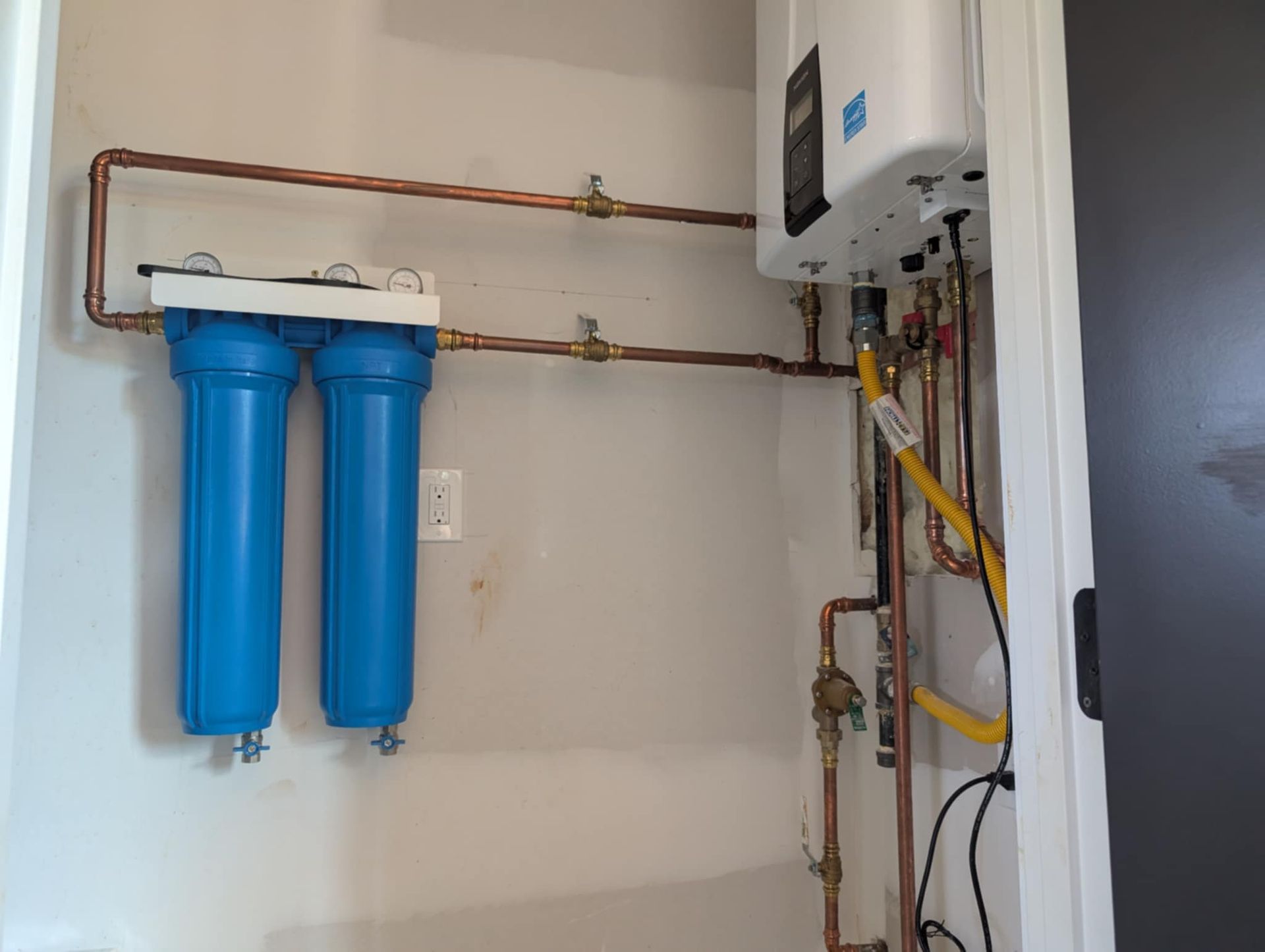 Home utility room with blue water filters, copper pipes, and a wall-mounted boiler.