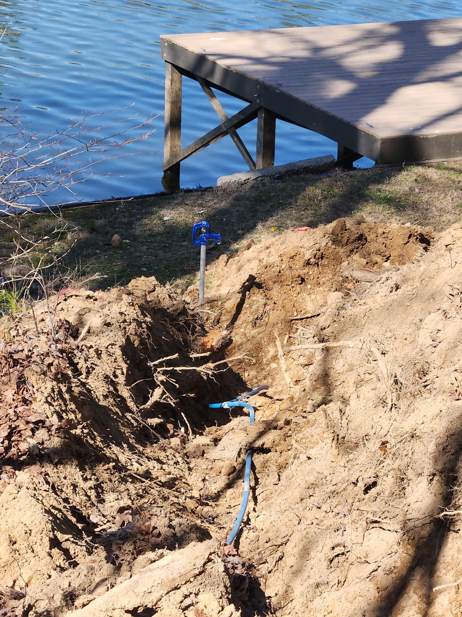 Blue pipe exposed in a sandy shoreline near a wooden dock beside calm water.