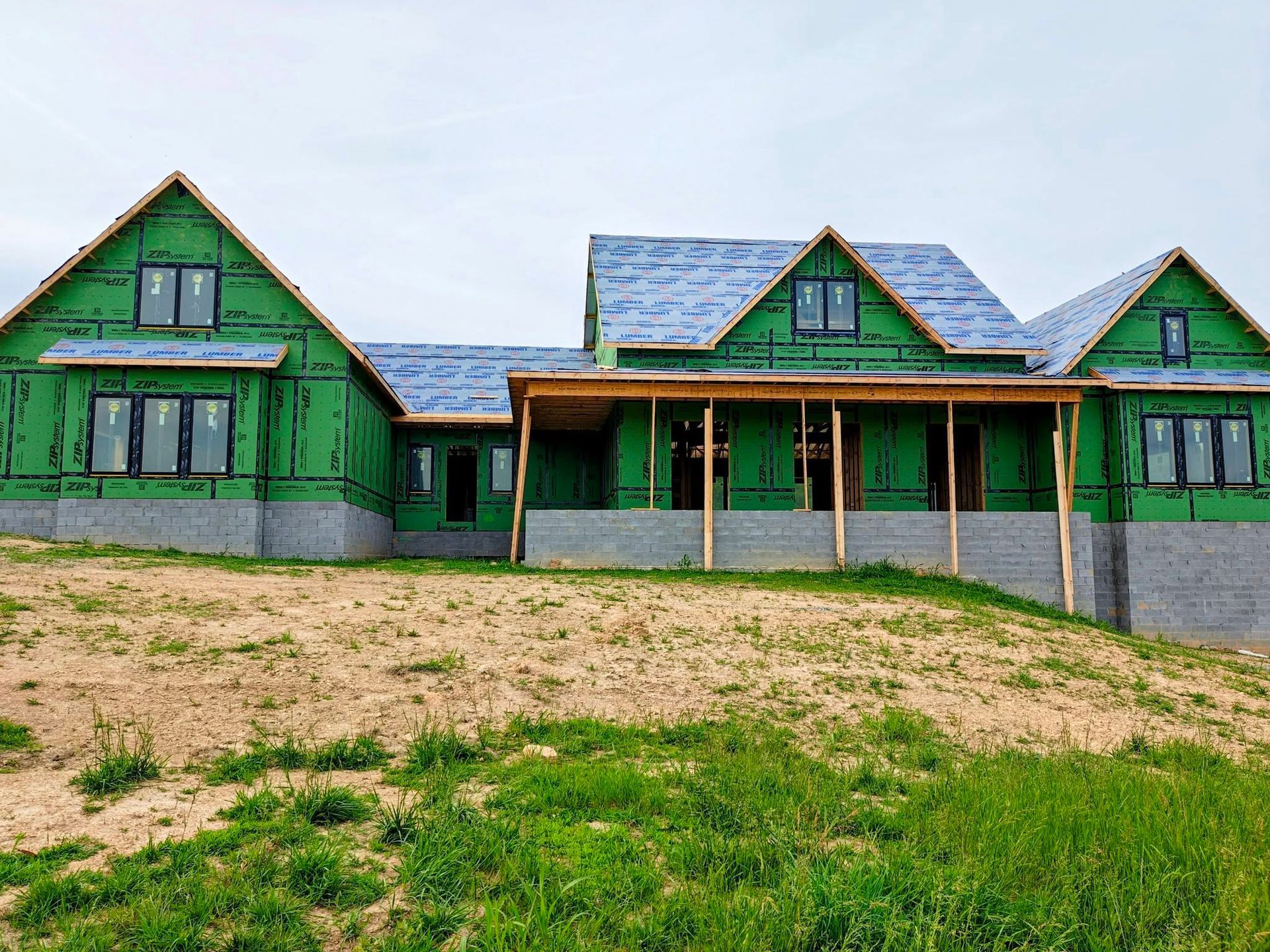 Green house with blue roof and front porch, viewed from a grassy yard