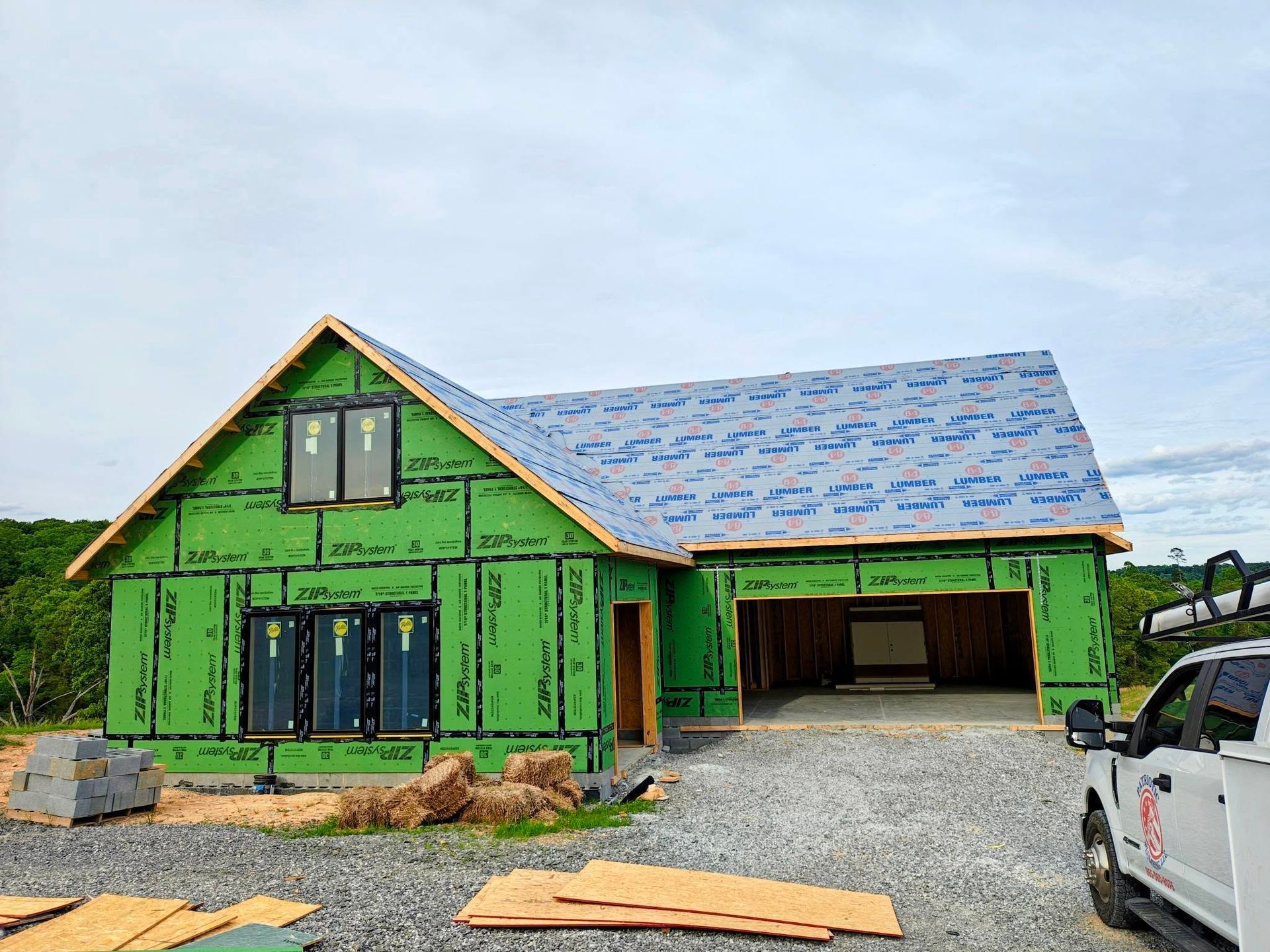 Bright green house under construction with blue roof, gravel lot, and a truck on the right