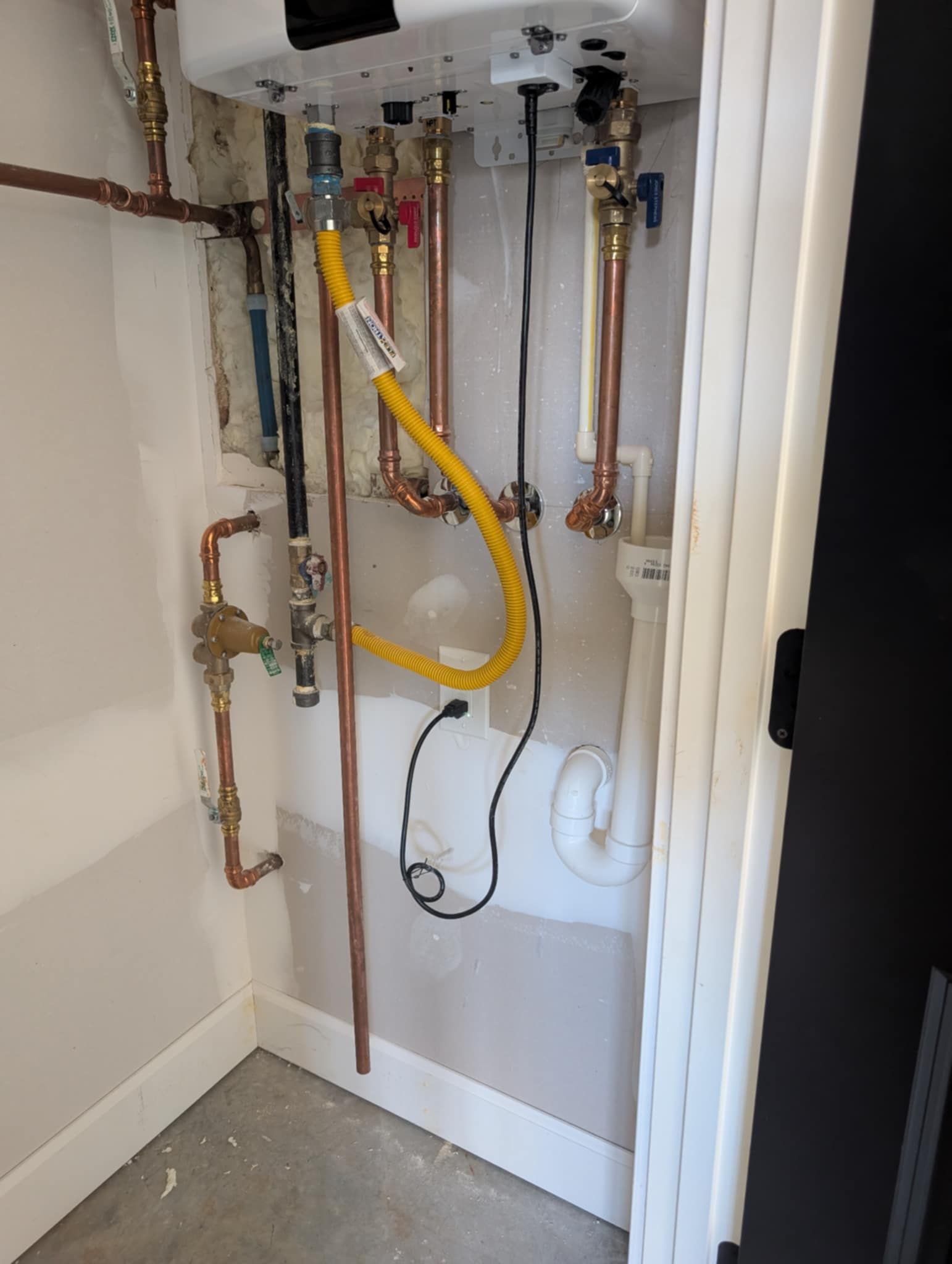 Open cabinet with exposed plumbing pipes, valves, and yellow flexible gas line under a sink.