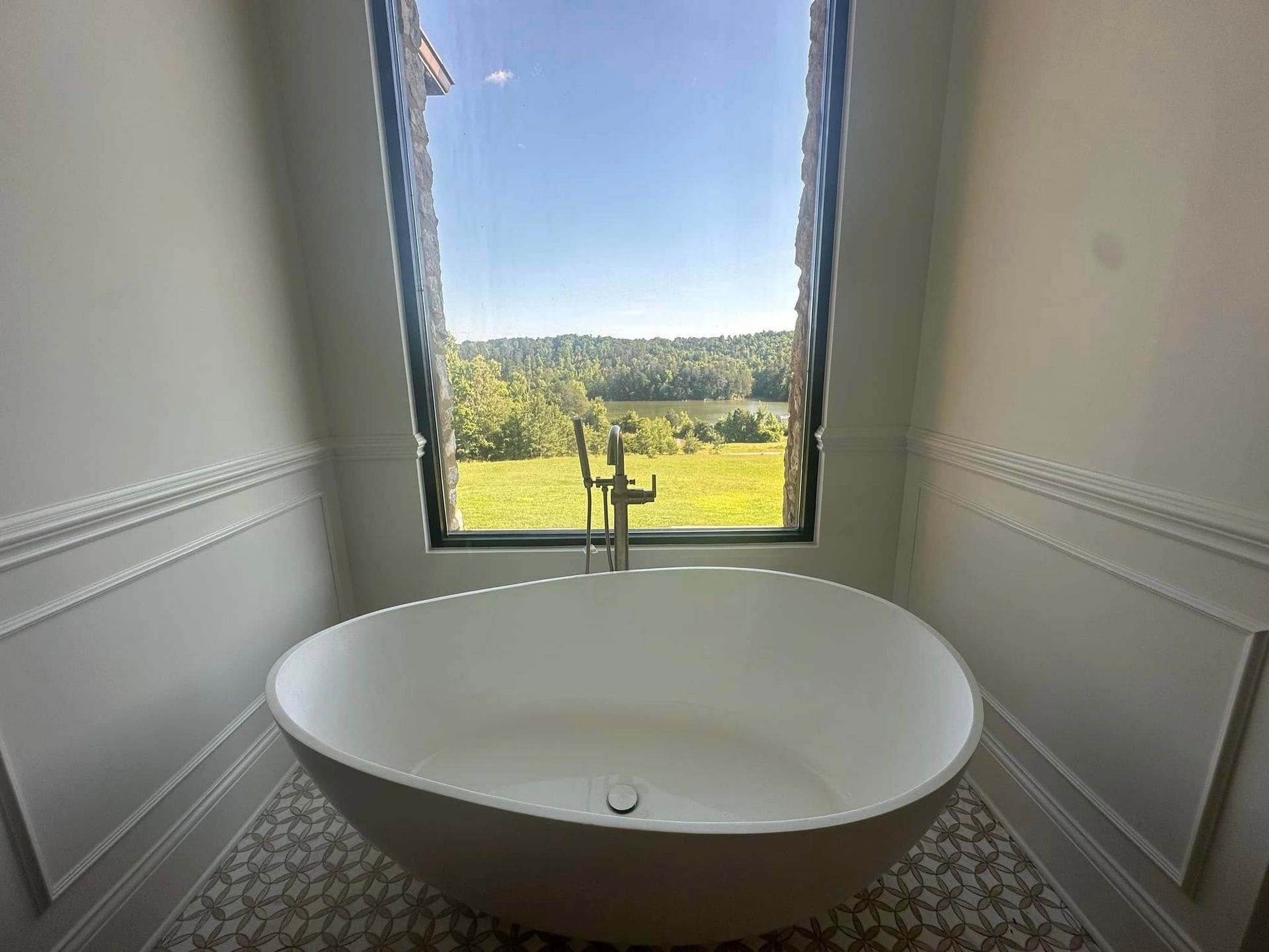 Freestanding white bathtub facing a window with a green landscape view.