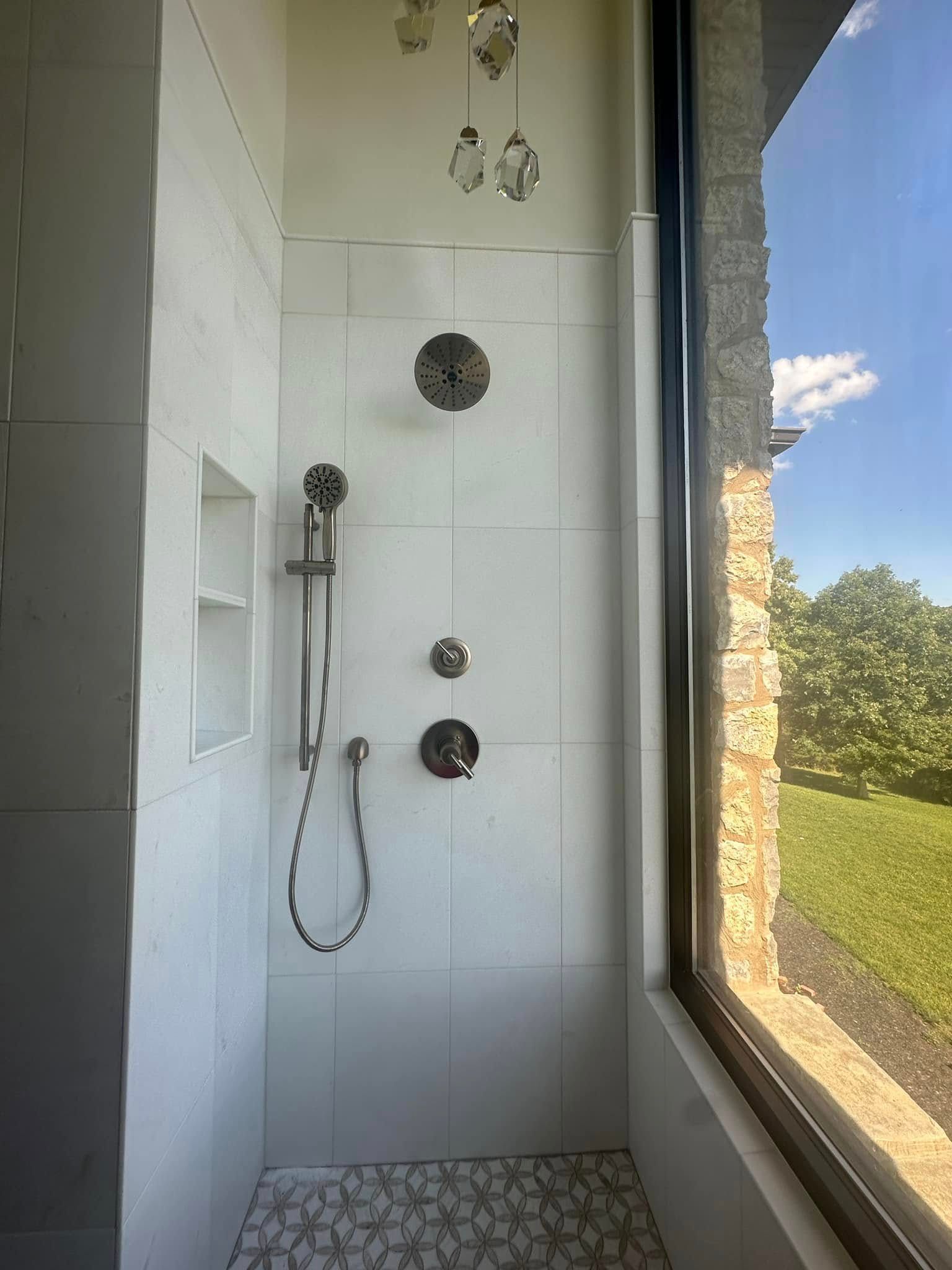 White tiled walk-in shower with chrome fixtures beside a large window overlooking greenery