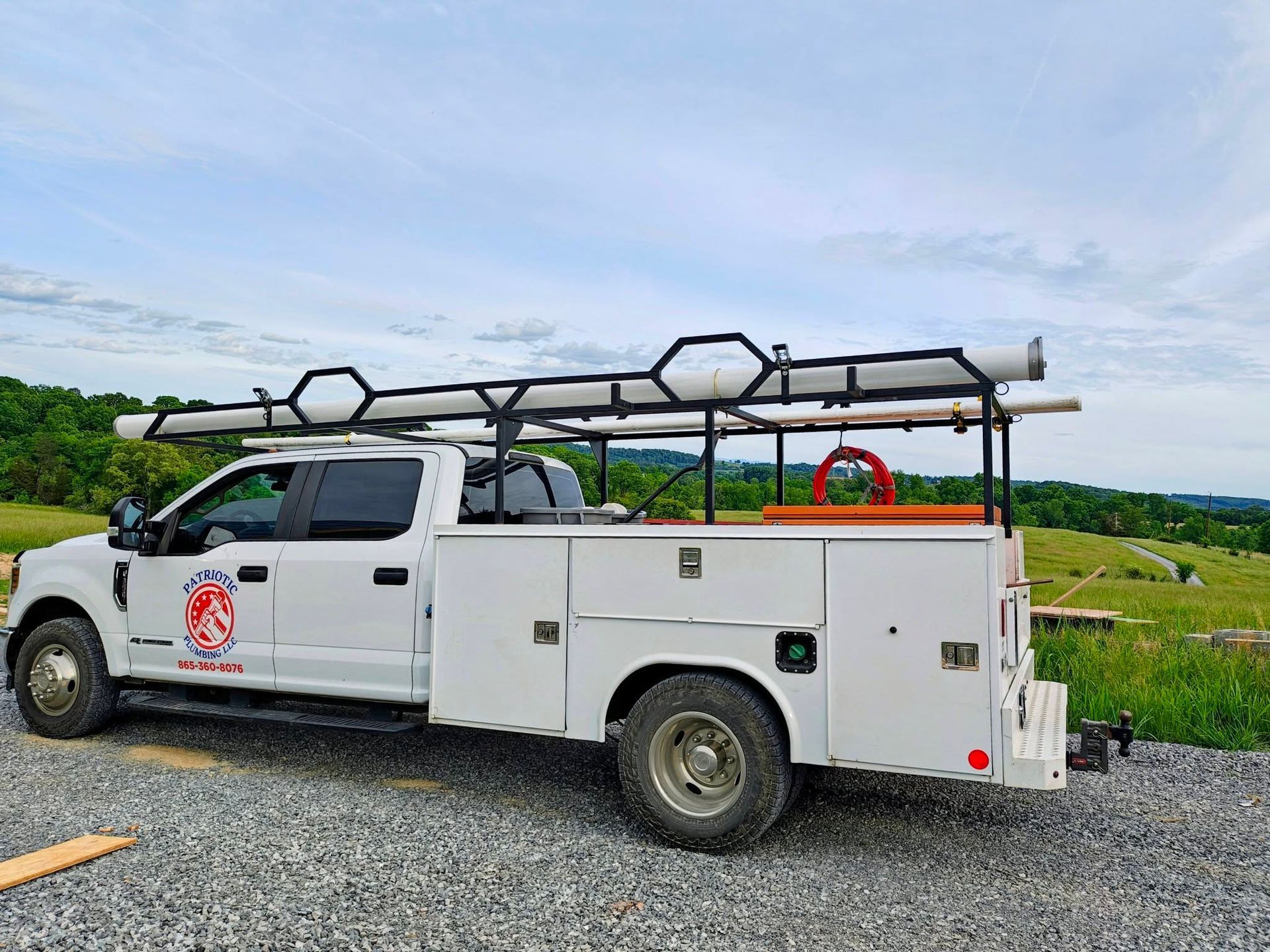 White utility truck with roof-mounted equipment parked on gravel beside green fields under a cloudy sky