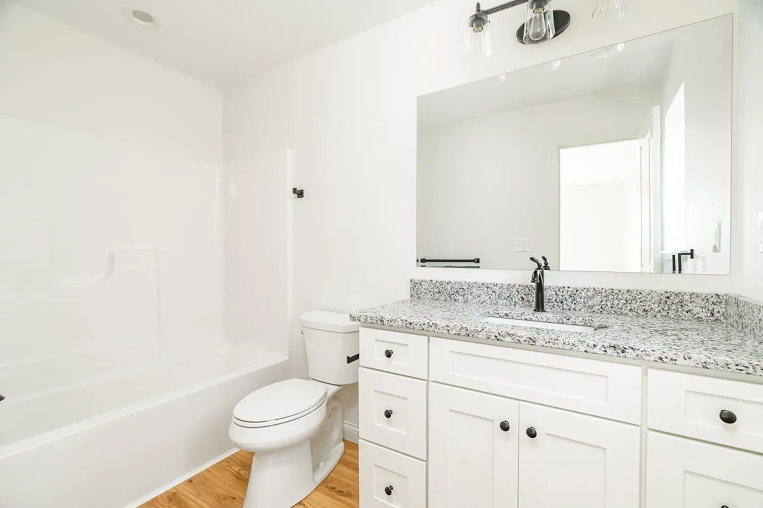 Bright white bathroom with tub, toilet, and vanity with large mirror