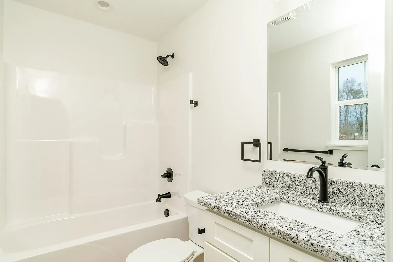 Bright bathroom with white tub, granite vanity, mirror, and window.