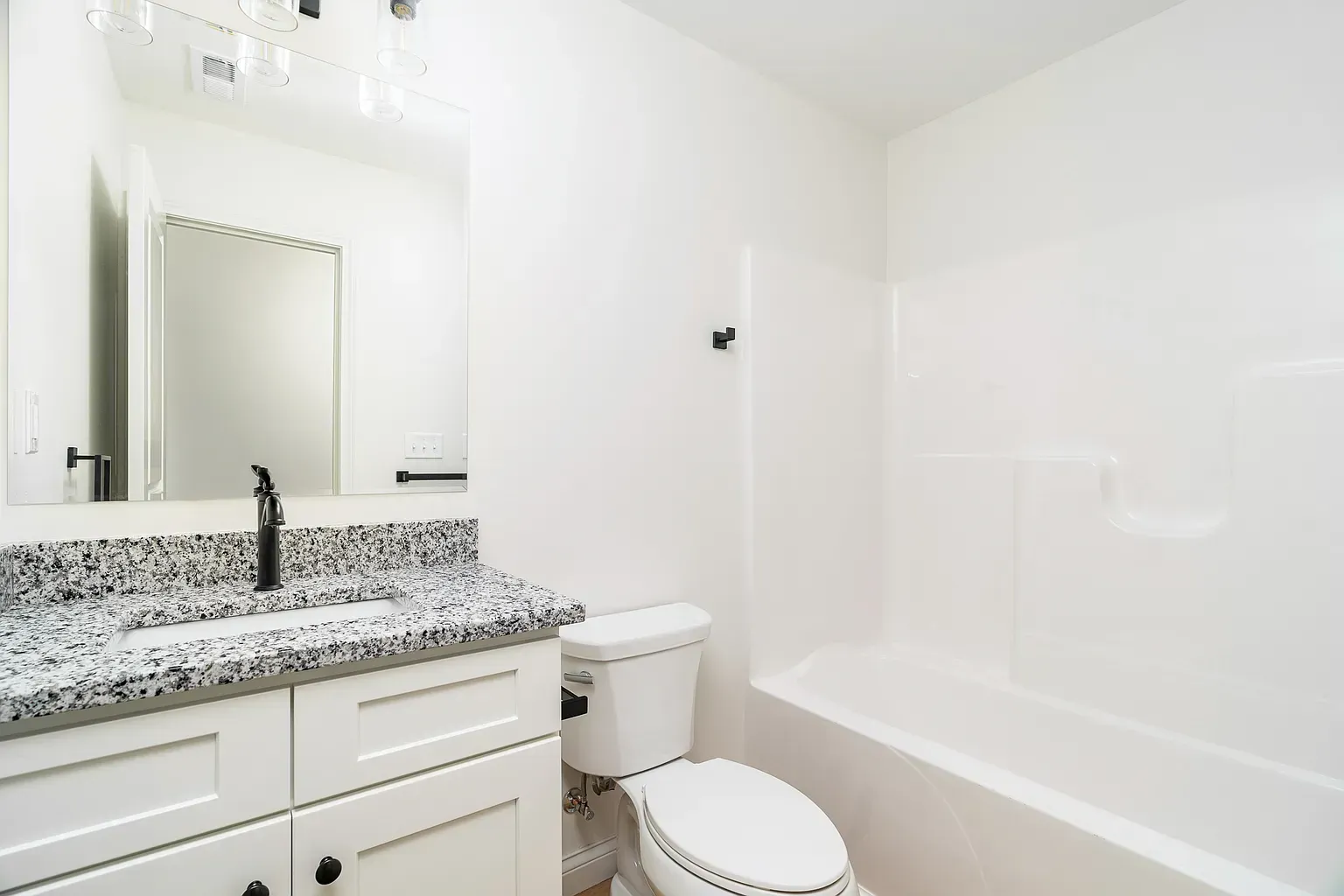 Bright white bathroom with granite vanity, mirror, toilet, and bathtub.
