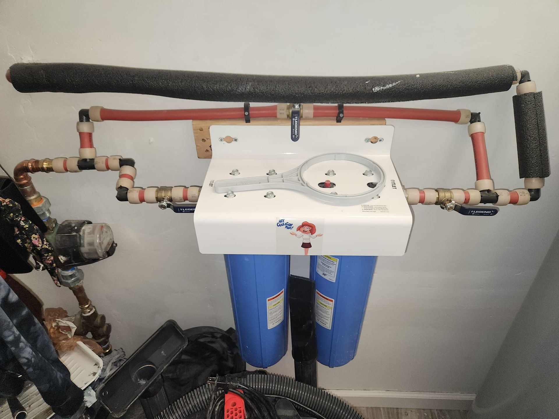 Residential plumbing setup with white control unit and blue filters beneath exposed pipes on a wall