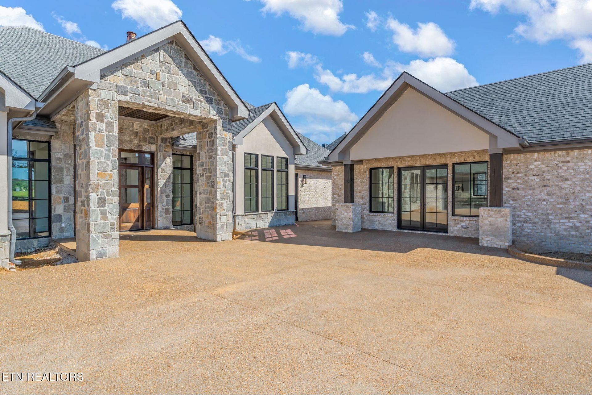 Luxury stone house with gabled roof and wide gravel driveway under a bright blue sky