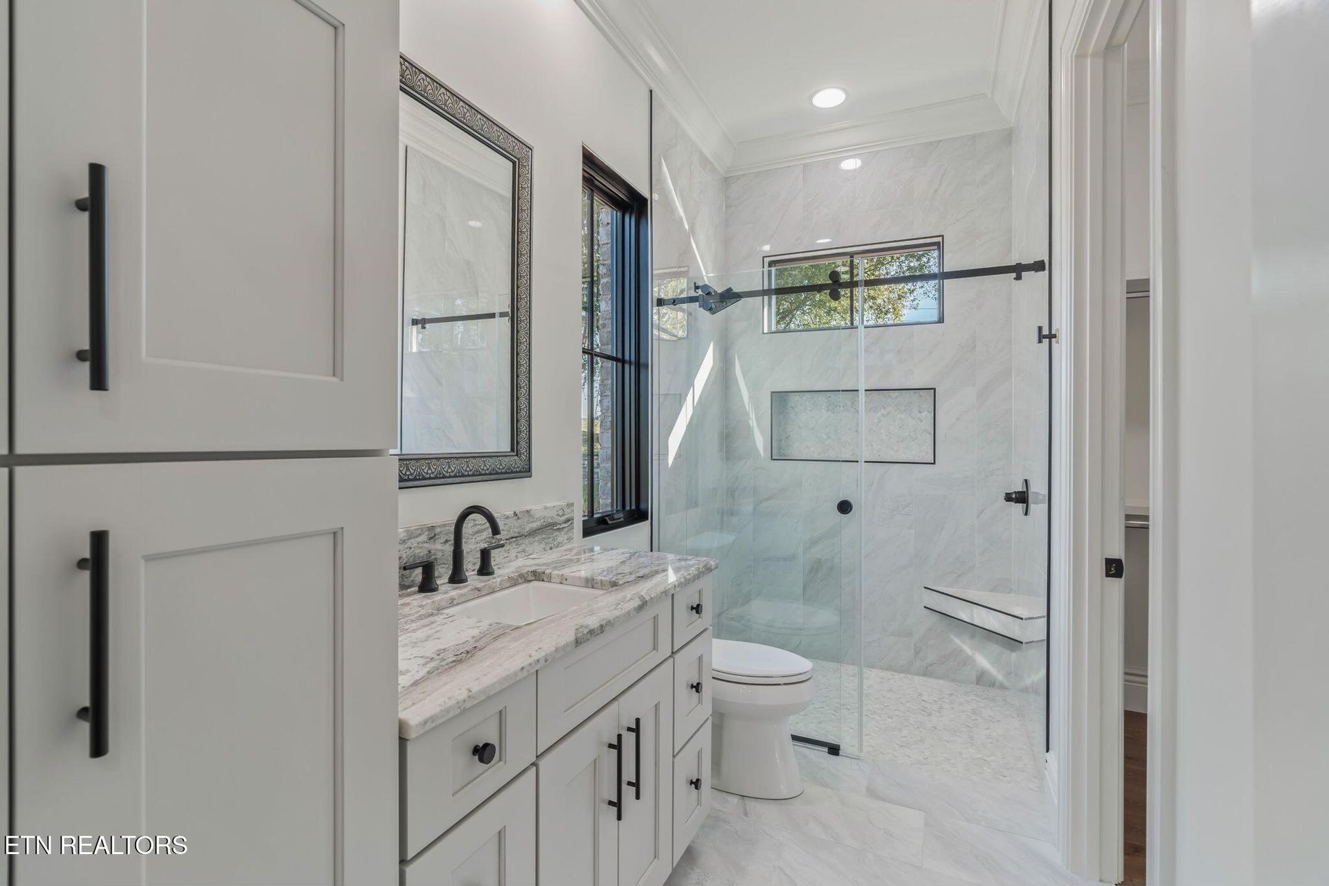 Bright white modern bathroom with double vanity, black fixtures, and glass shower door