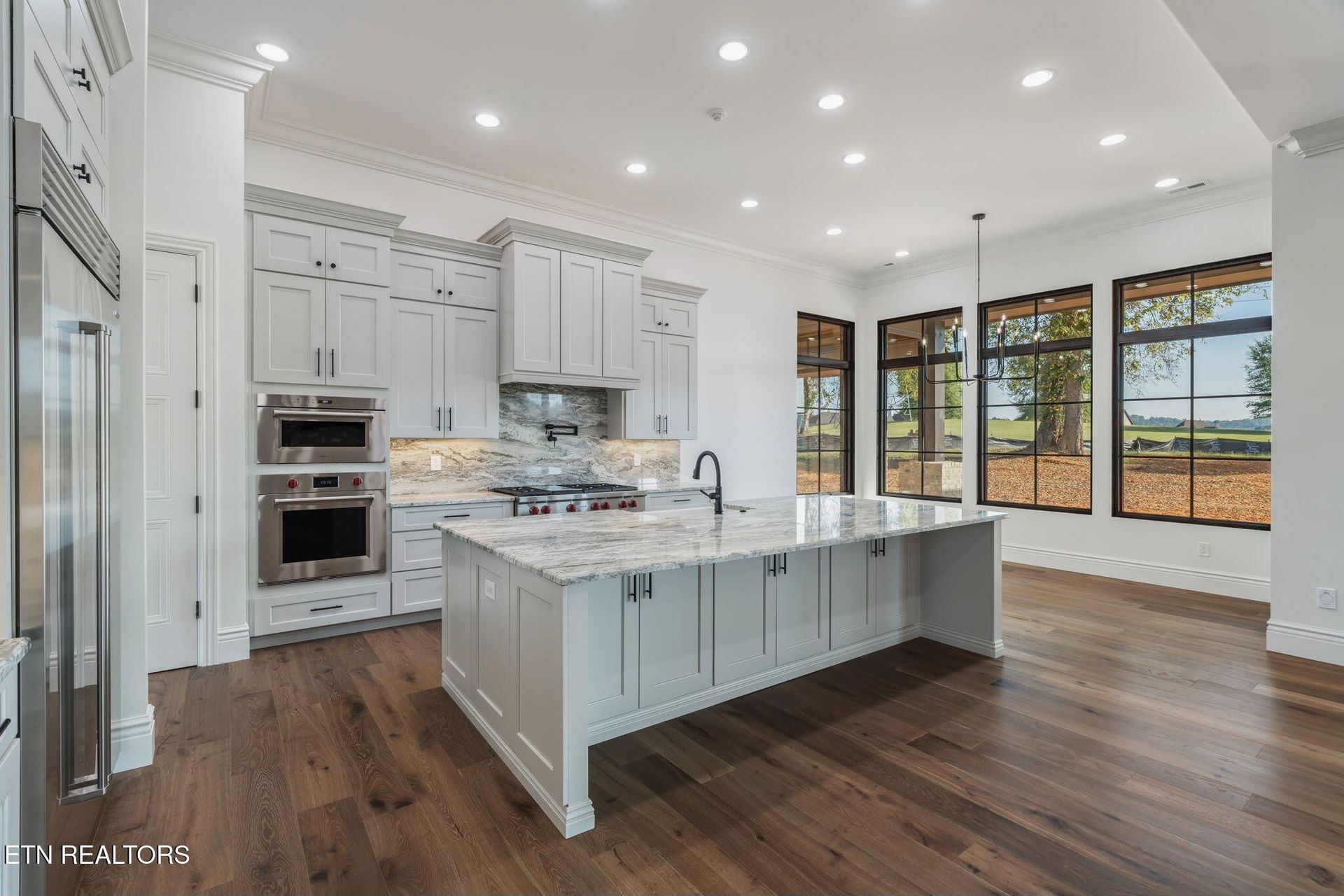 Bright modern kitchen with white cabinets, large island, dark wood floors, and floor-to-ceiling windows