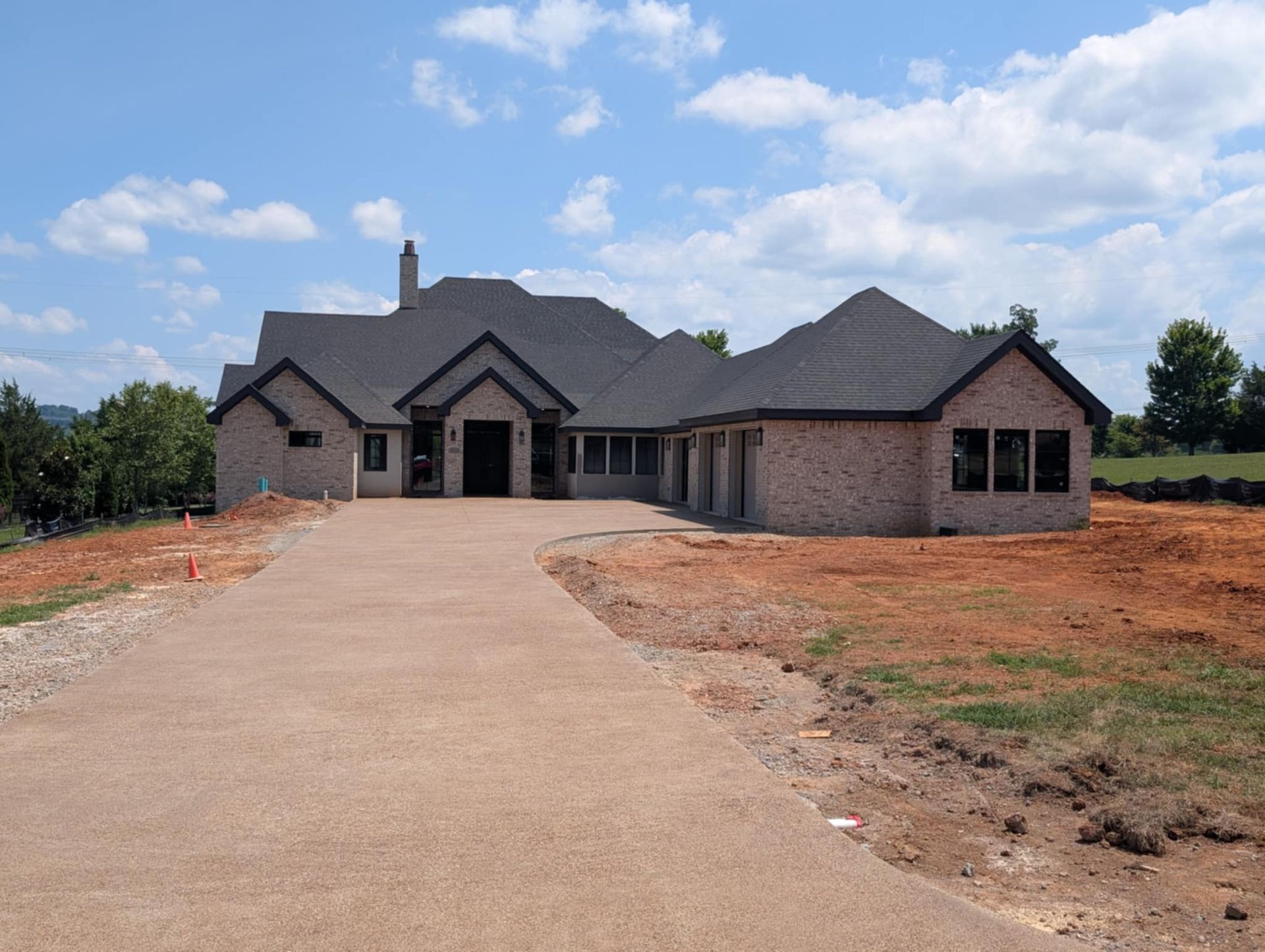 New brick house with a long driveway and unfinished front yard under a partly cloudy sky