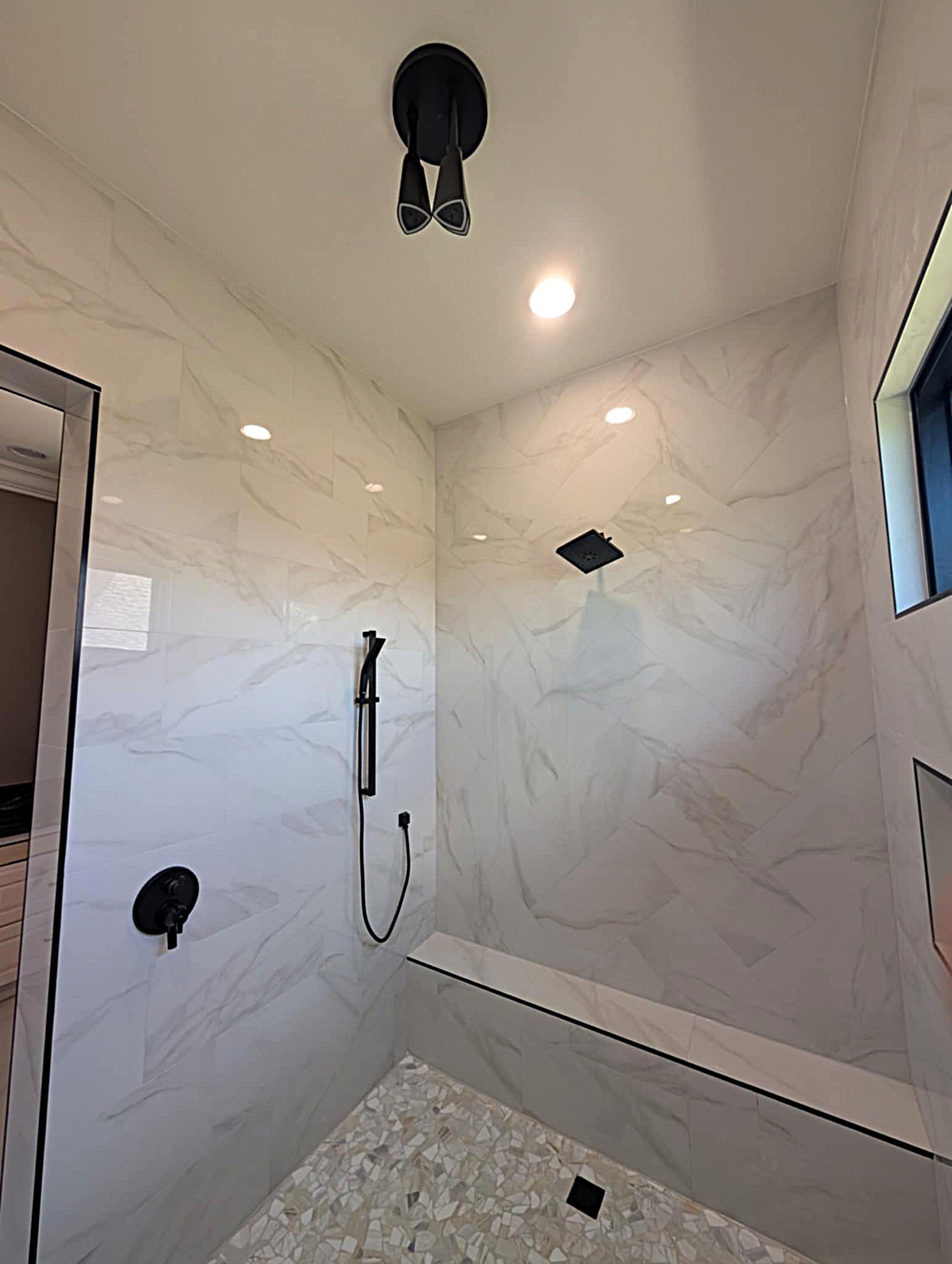 White-tiled walk-in shower with black fixtures, rain showerhead, handheld sprayer, and linear drain.