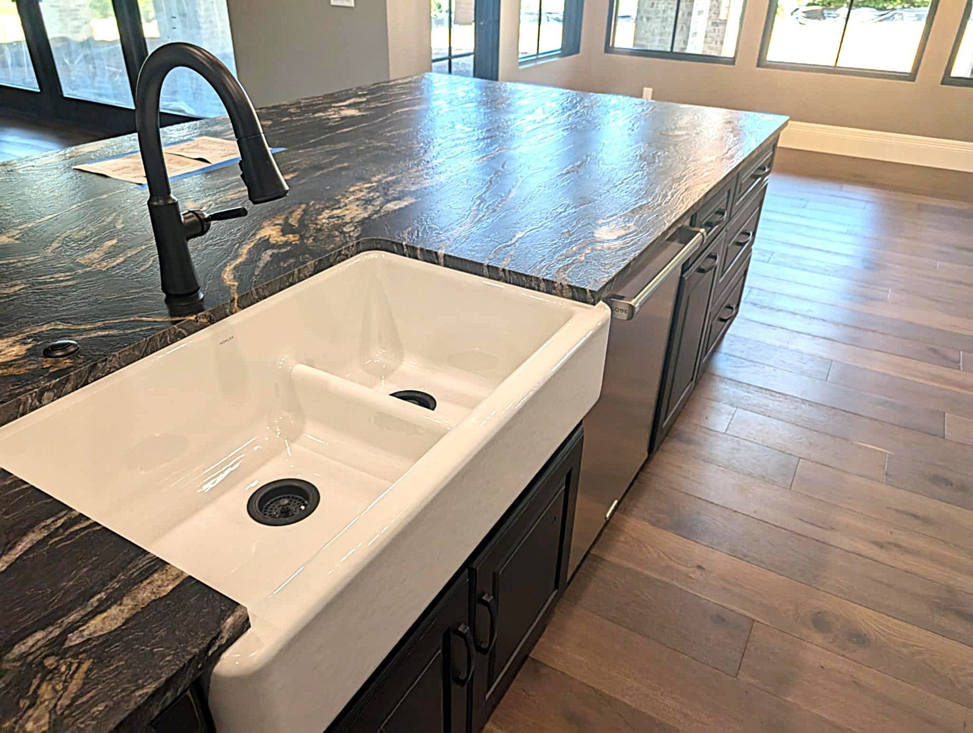 White farmhouse sink in a dark stone kitchen island with black faucet and wood floors.