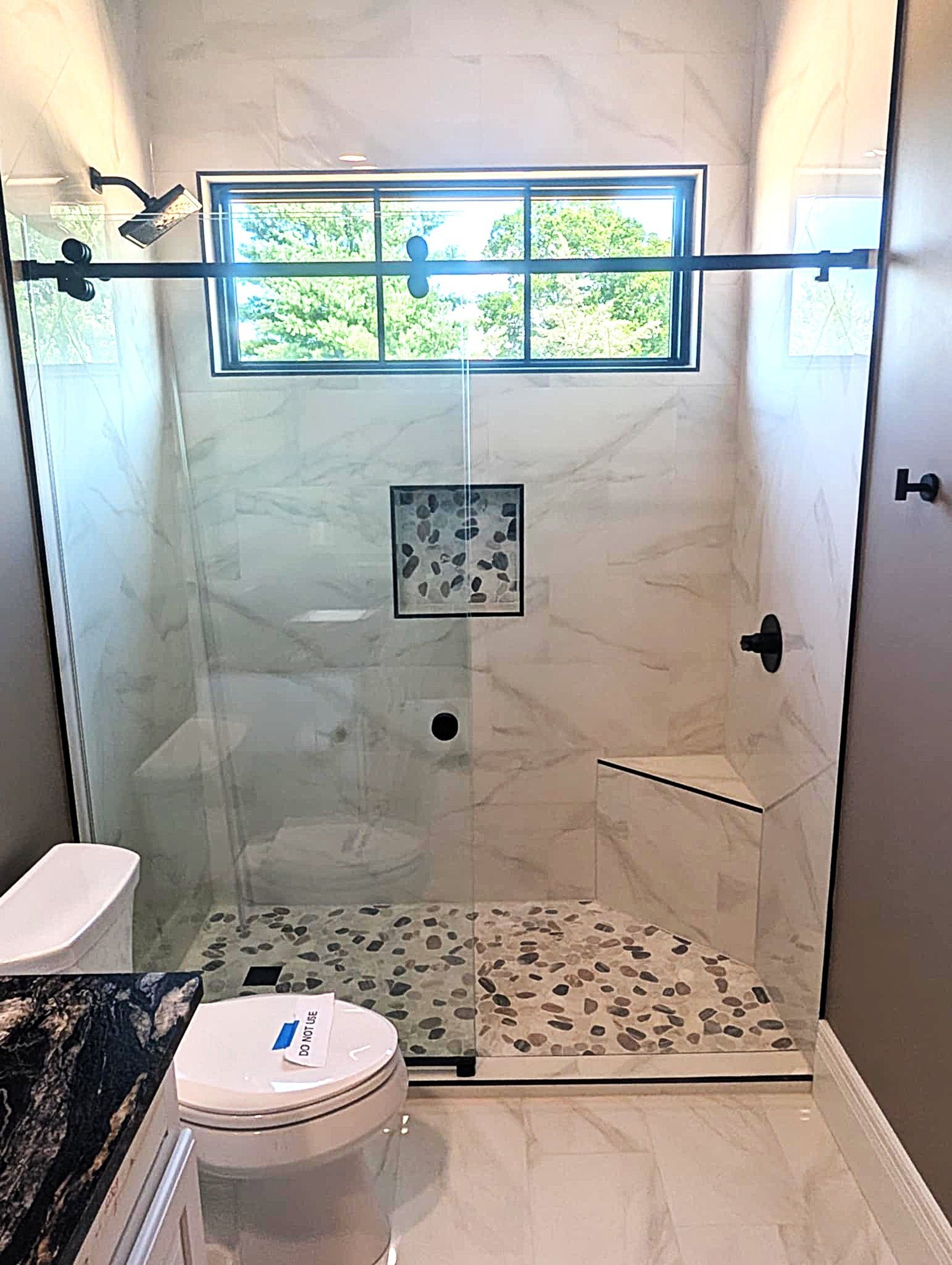 Bathroom with a tiled shower, glass door, window, and toilet visible in front.