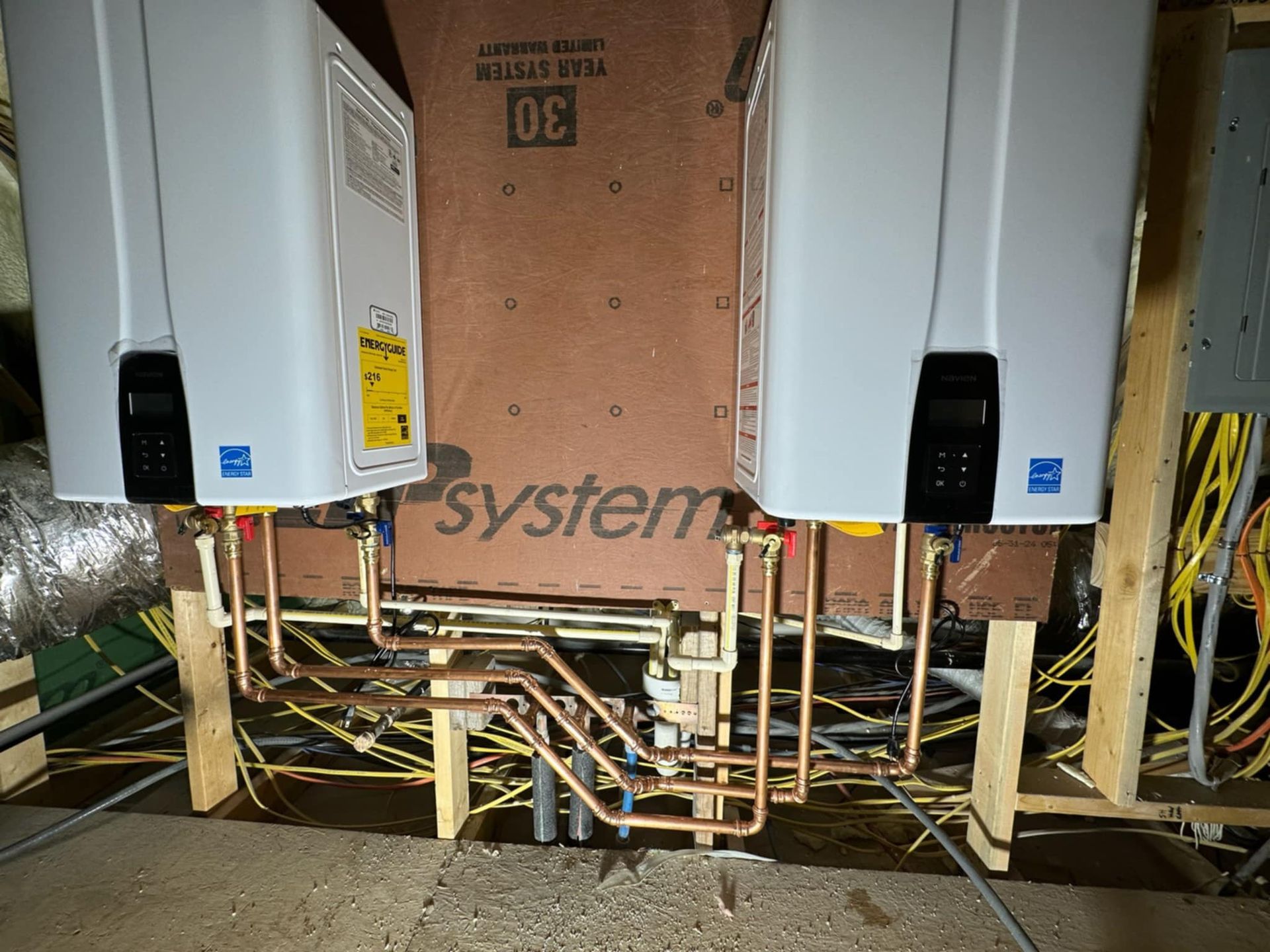 Two white utility boxes and exposed copper pipes inside a wall cavity with pink insulation board.