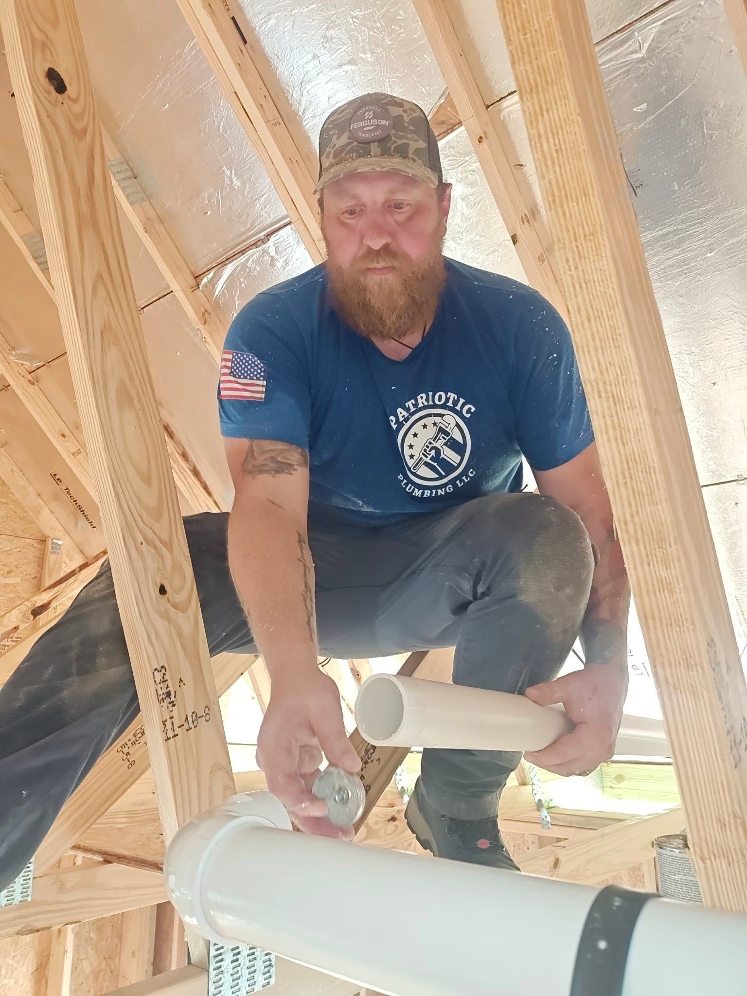 Worker crouching in a wooden frame, measuring a white PVC pipe during construction.