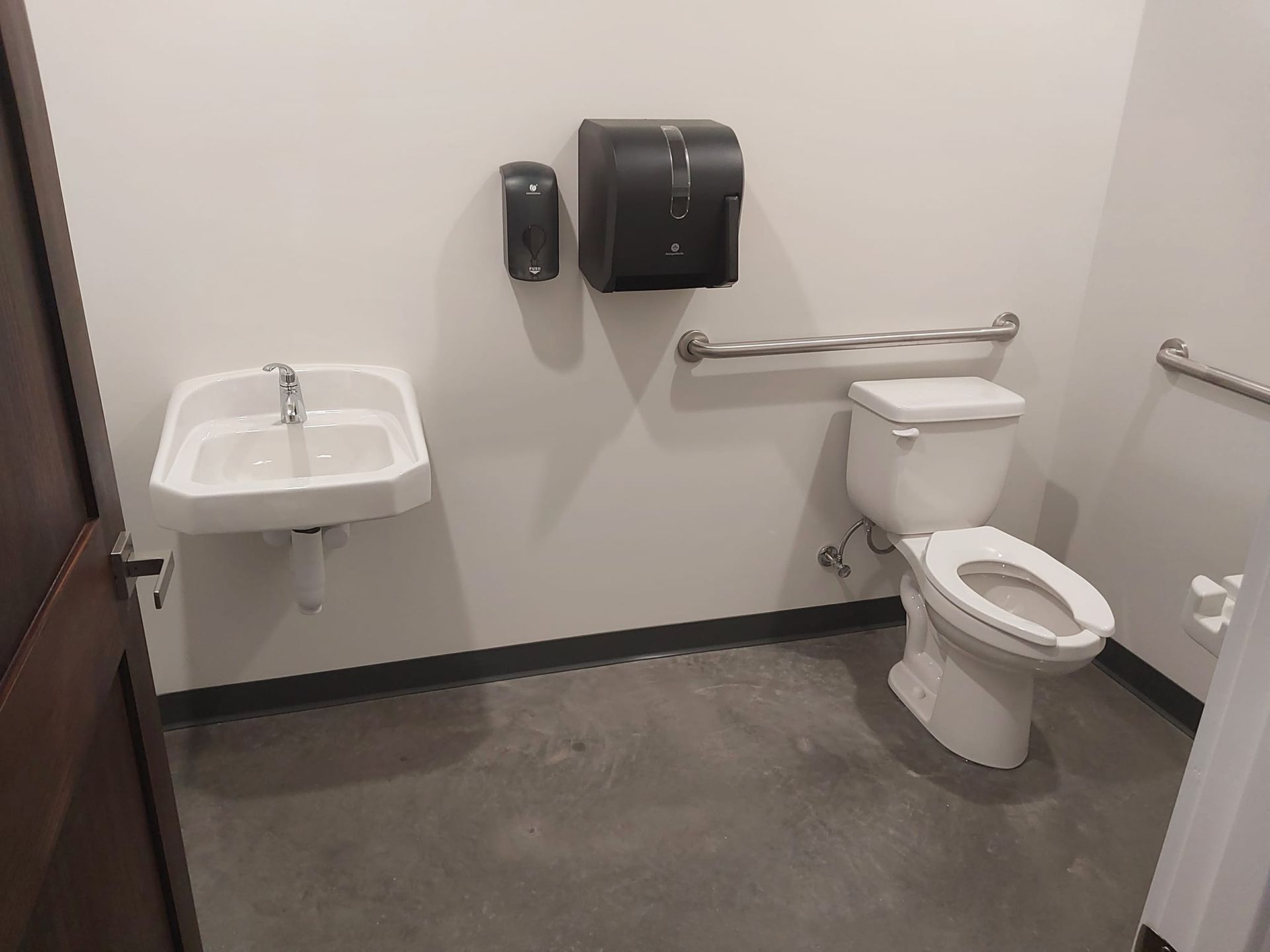 Accessible bathroom with sink, toilet, grab bars, and wall-mounted dispensers.