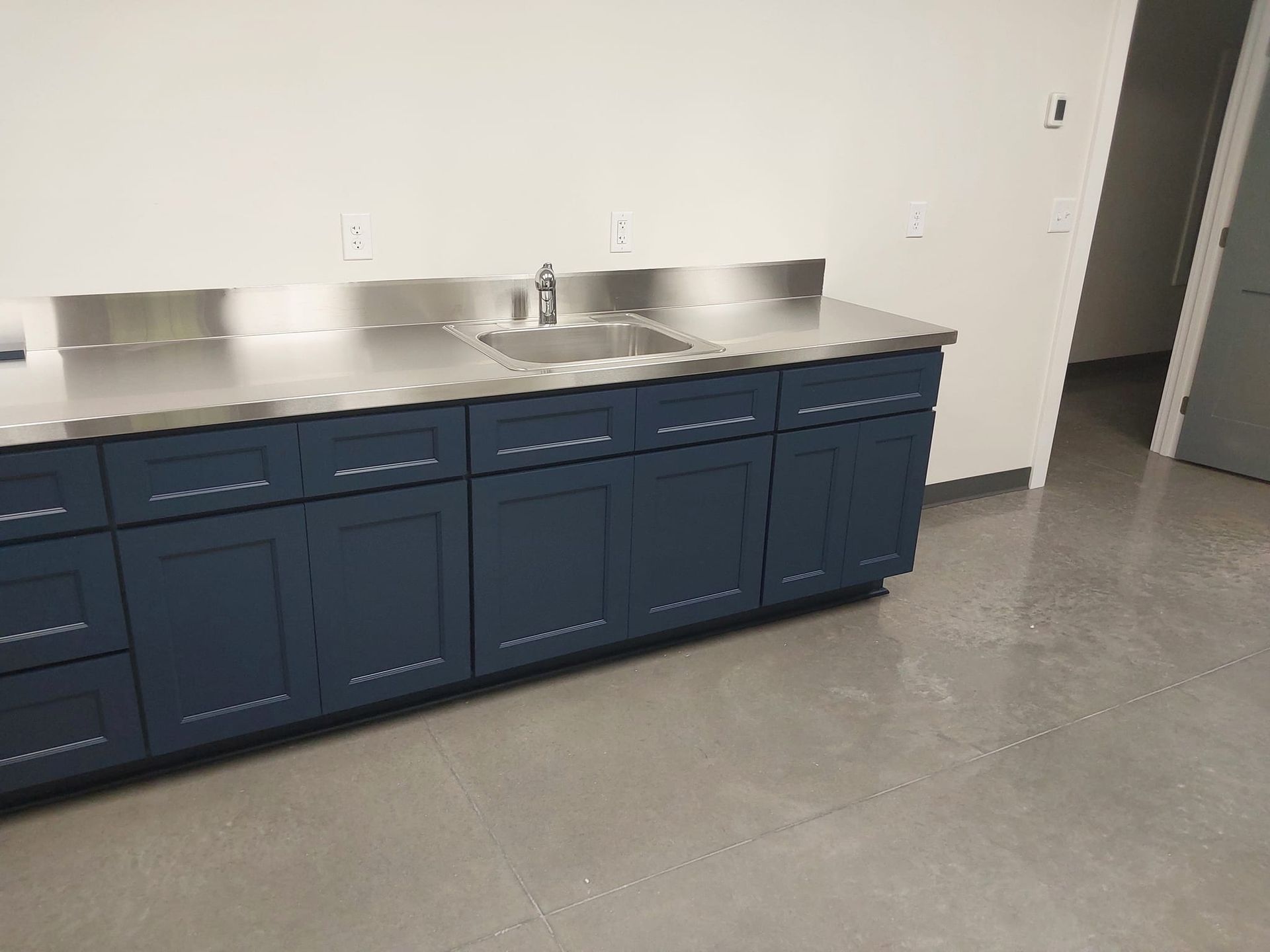 Blue cabinets with a stainless-steel countertop in an empty room with a gray floor.