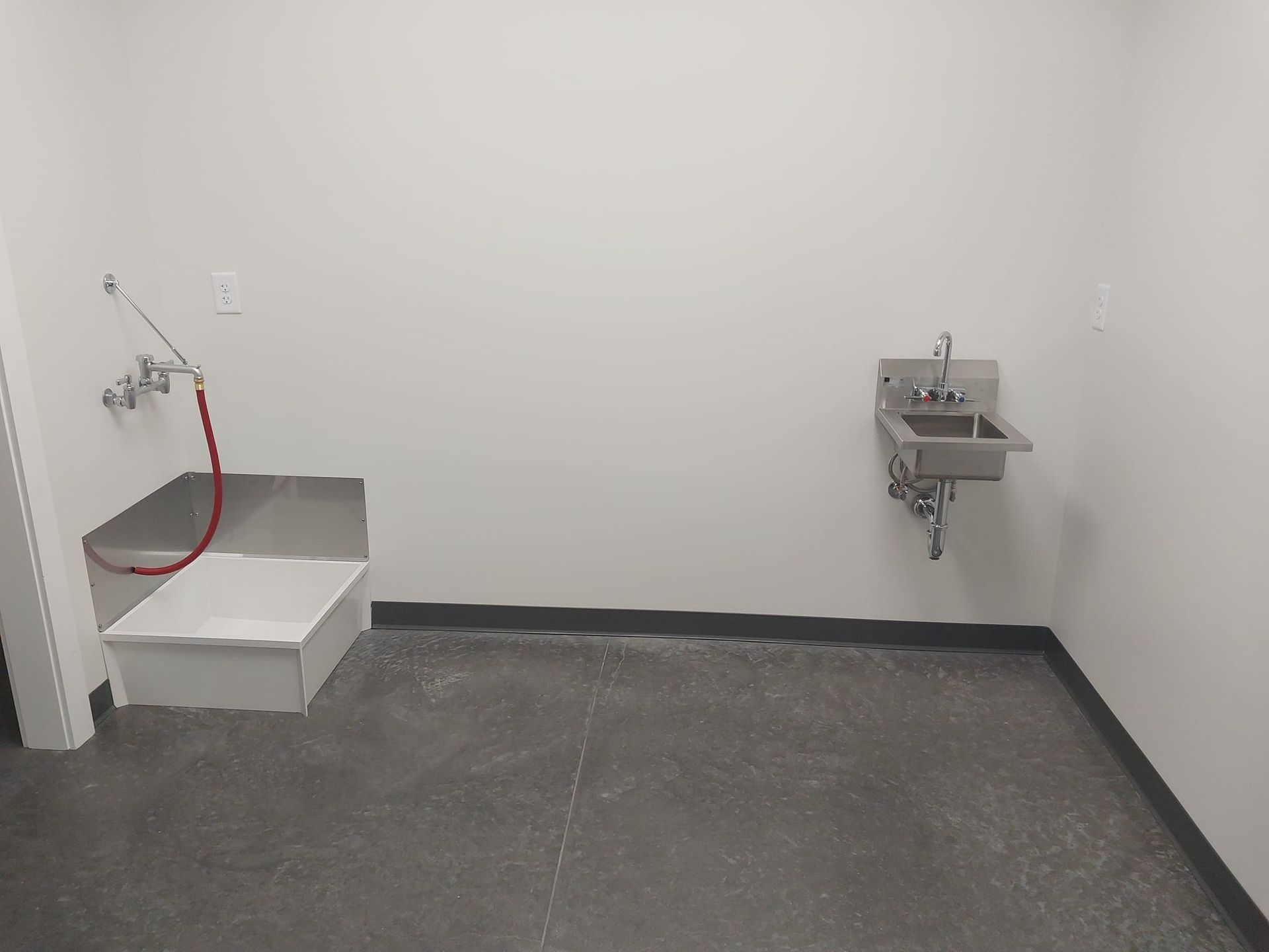 Small utility room with concrete floor, mop sink, and wall-mounted sink basin.